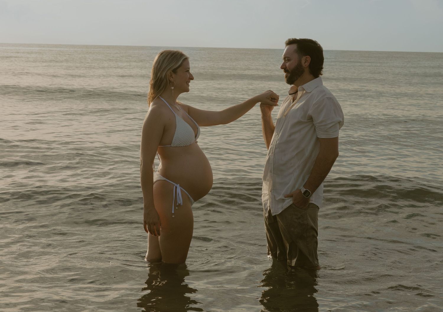 A couple stands together in calm ocean waters at sunset sharing an intimate moment at the beach.