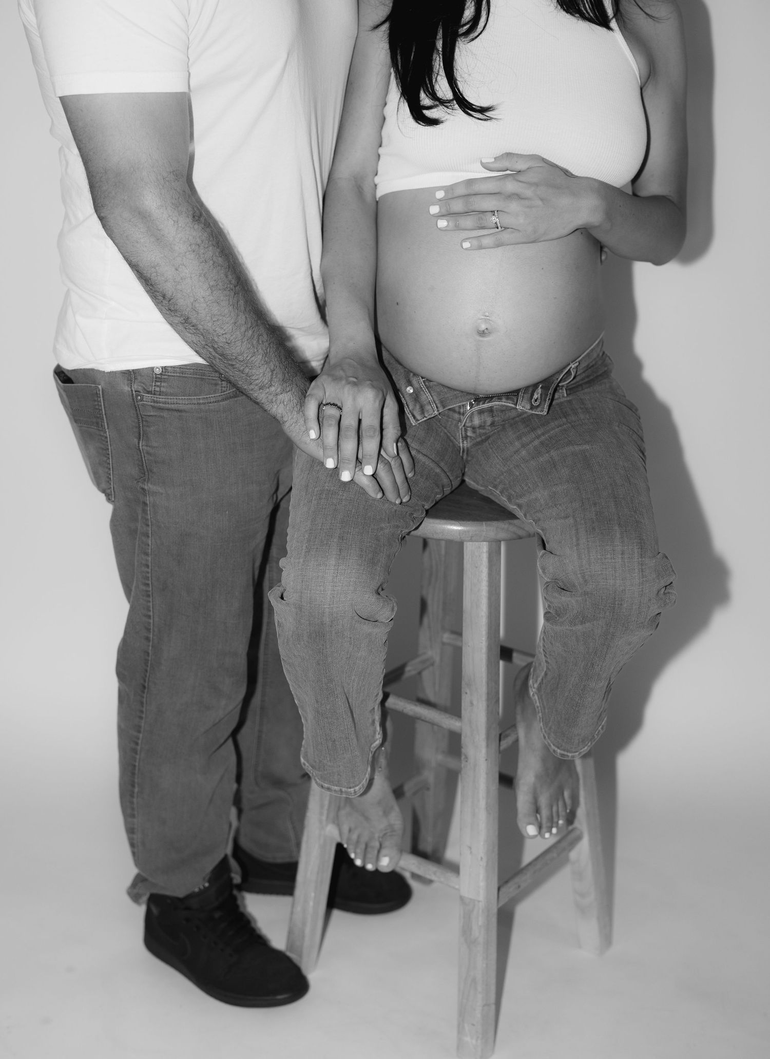 Black and white photo of two people sitting together on a wooden stool in casual attire.