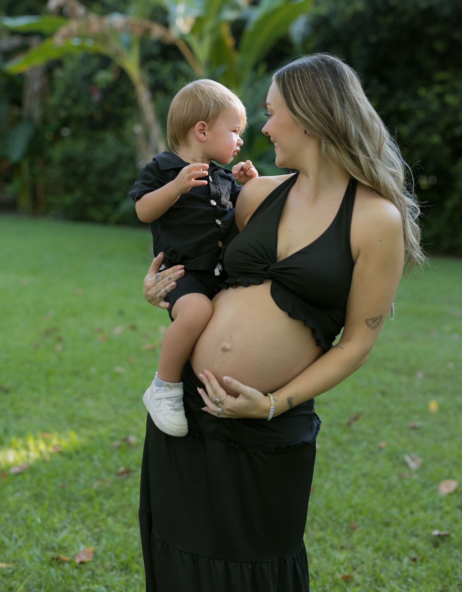 Family portraits taken in a lush green garden setting showing intimate moments between parent and child.
