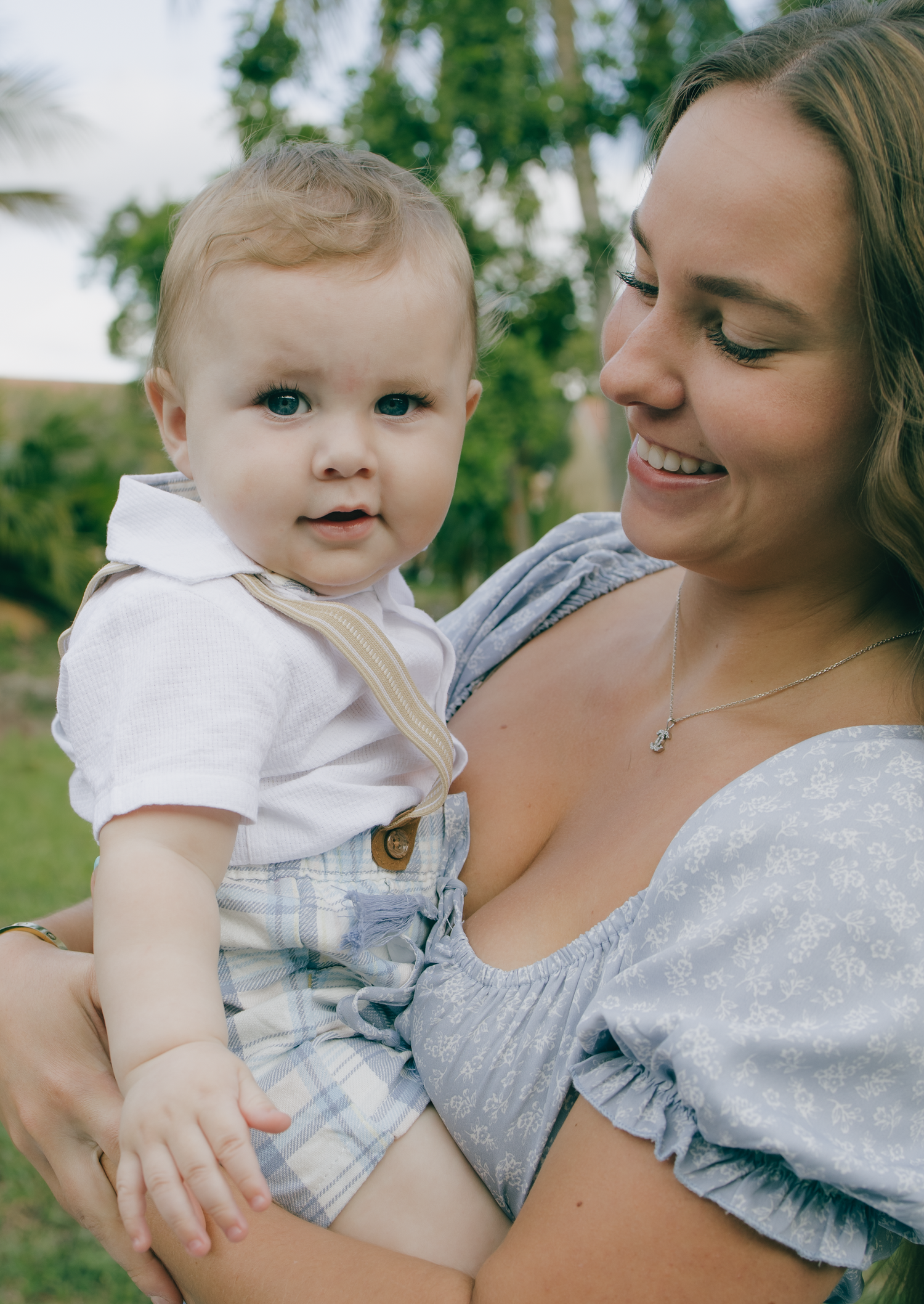 A joyful outdoor portrait of a mother and baby against a green garden background.
