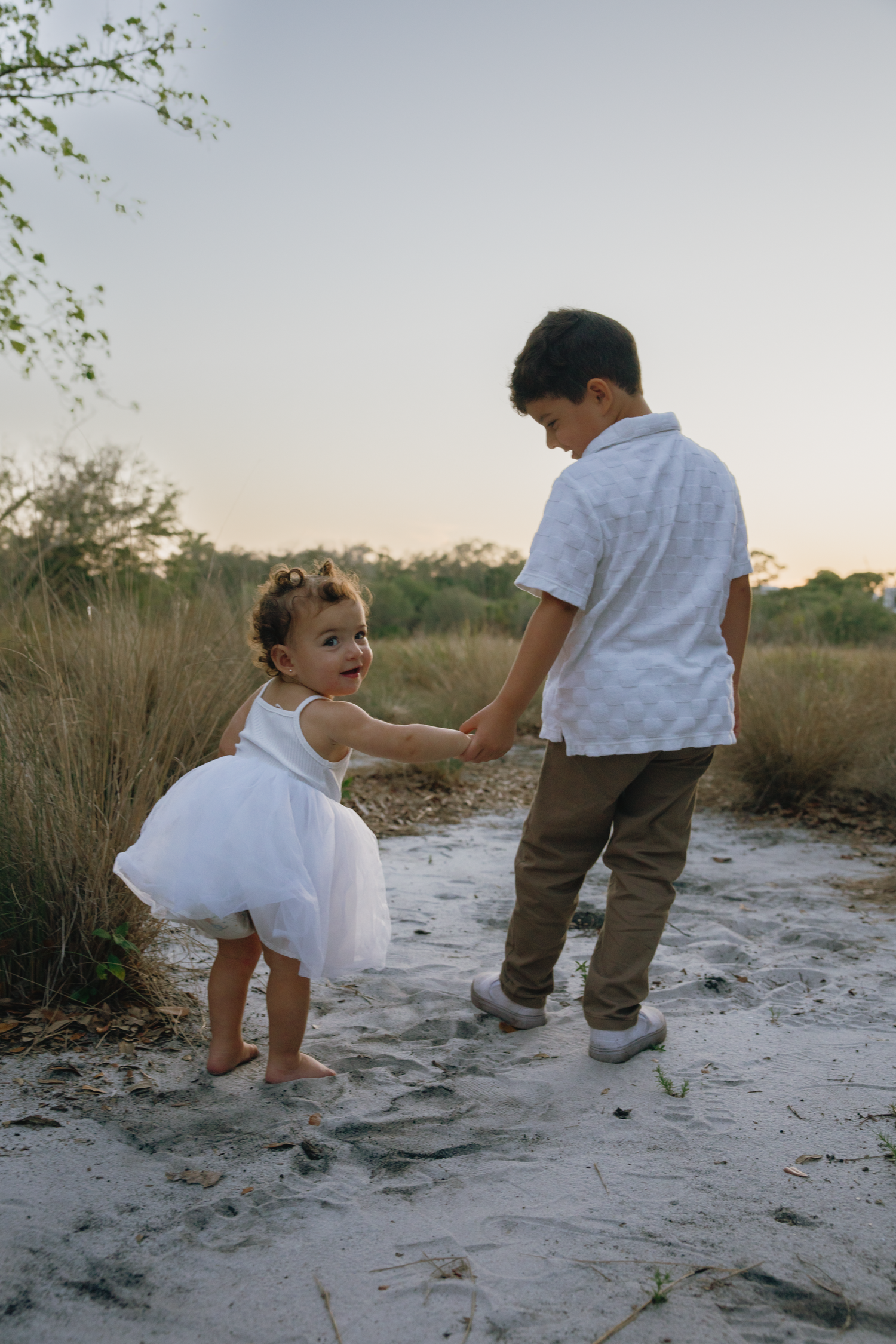 Two children playing together on a sandy path during sunset.
