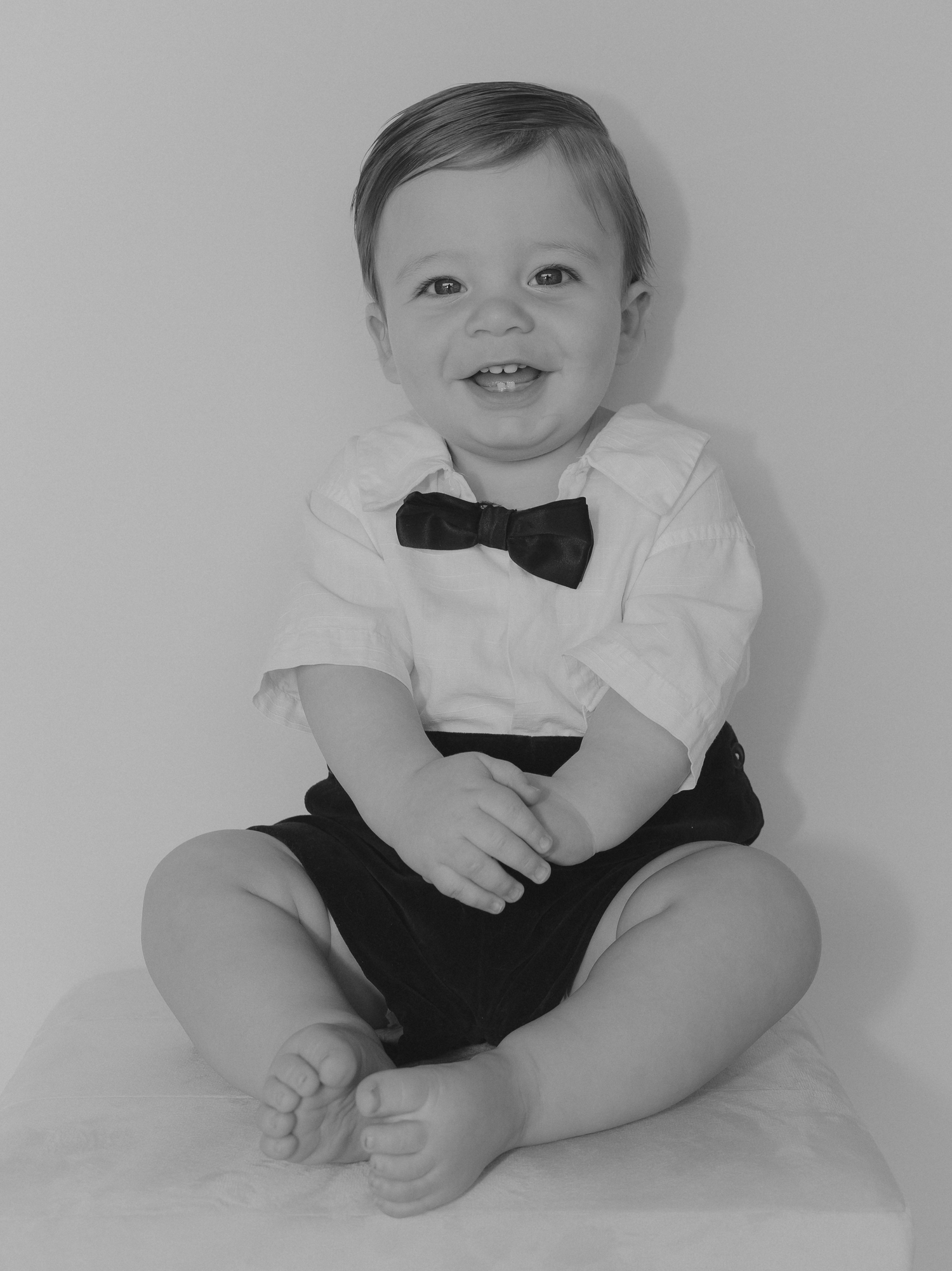 A baby in a black and white outfit smiles while lying on a white background in a series of four similar poses.