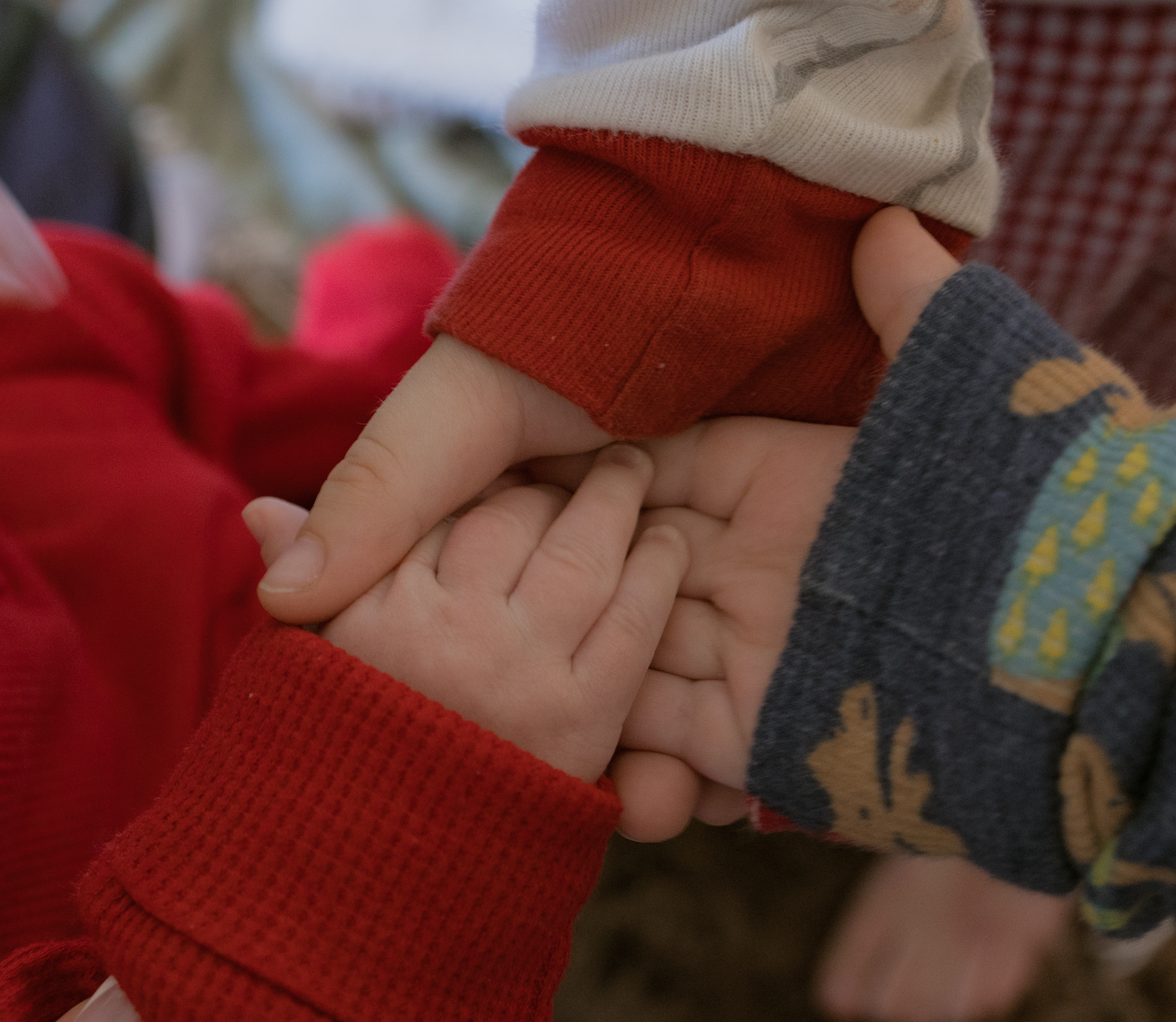 Three hands stacked together showing unity and connection against red and plaid fabric background.