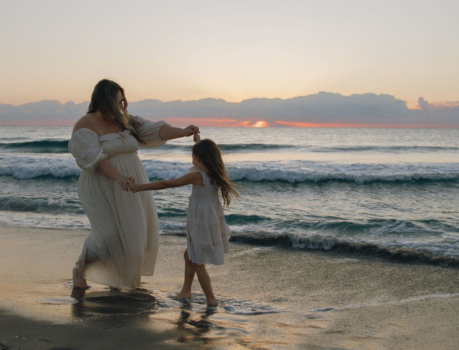 A parent and child play together at the beach during sunset with waves rolling in behind them.