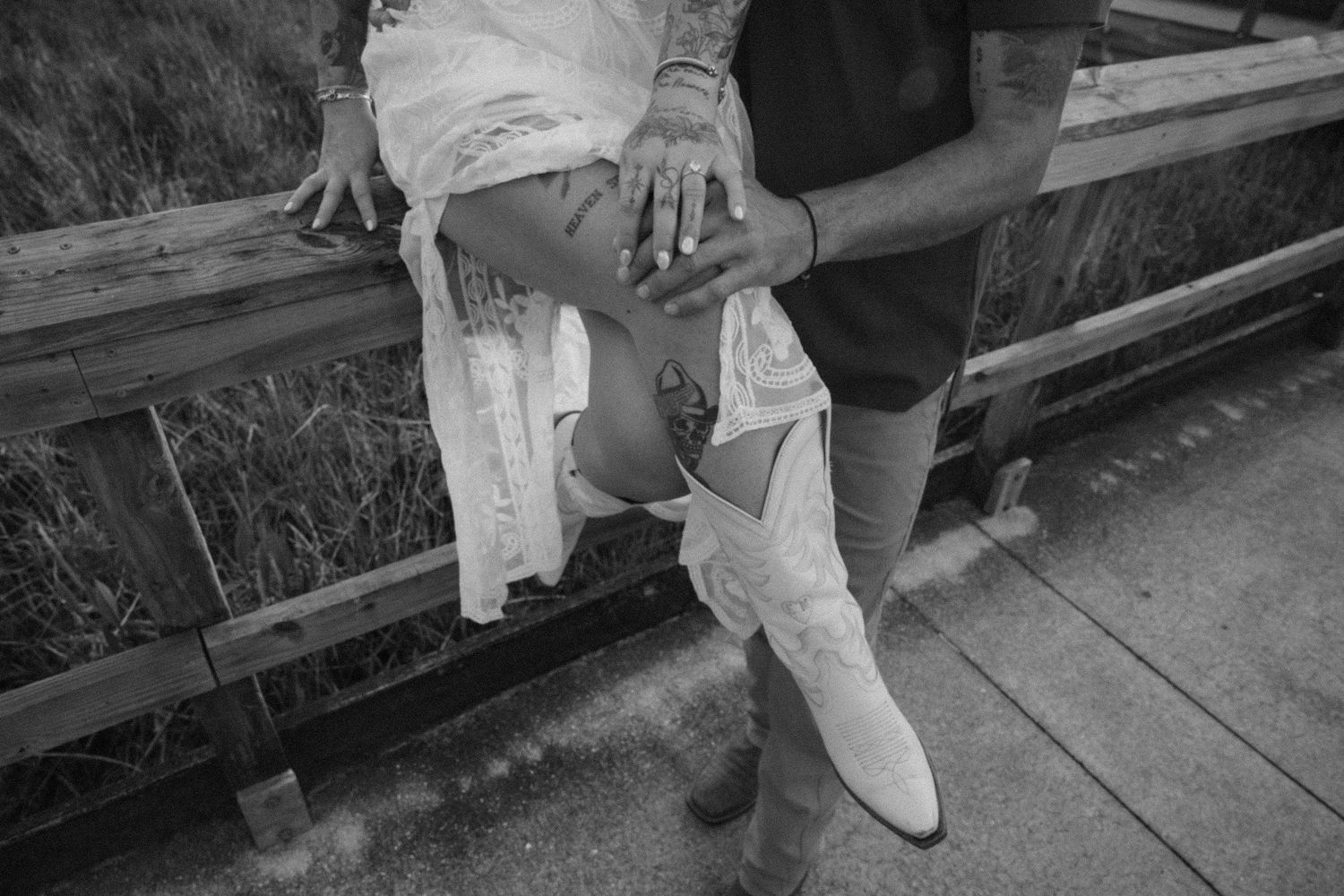 A black and white detail shot of white boots and casual attire on a wooden boardwalk.