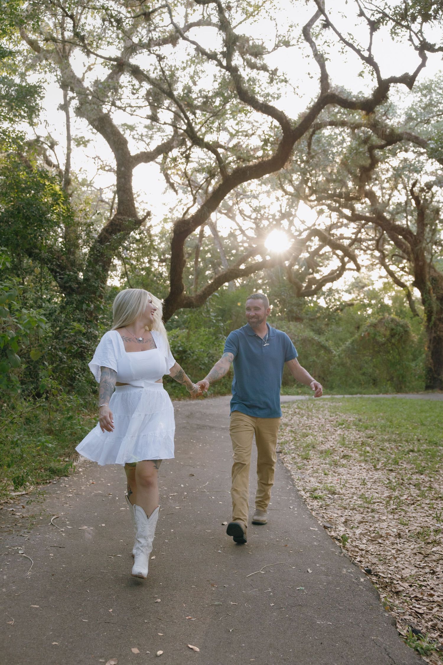 A couple walks together on a tree-lined path during sunset, playfully enjoying each other's company.