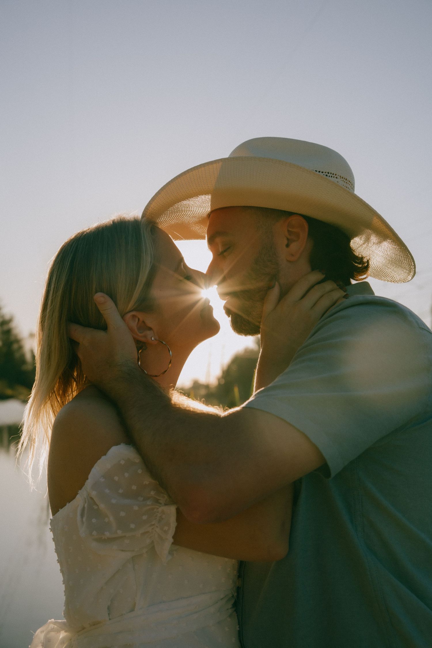 Silhouetted couple share romantic kisses against a bright sunlit sky while wearing cowboy hats.