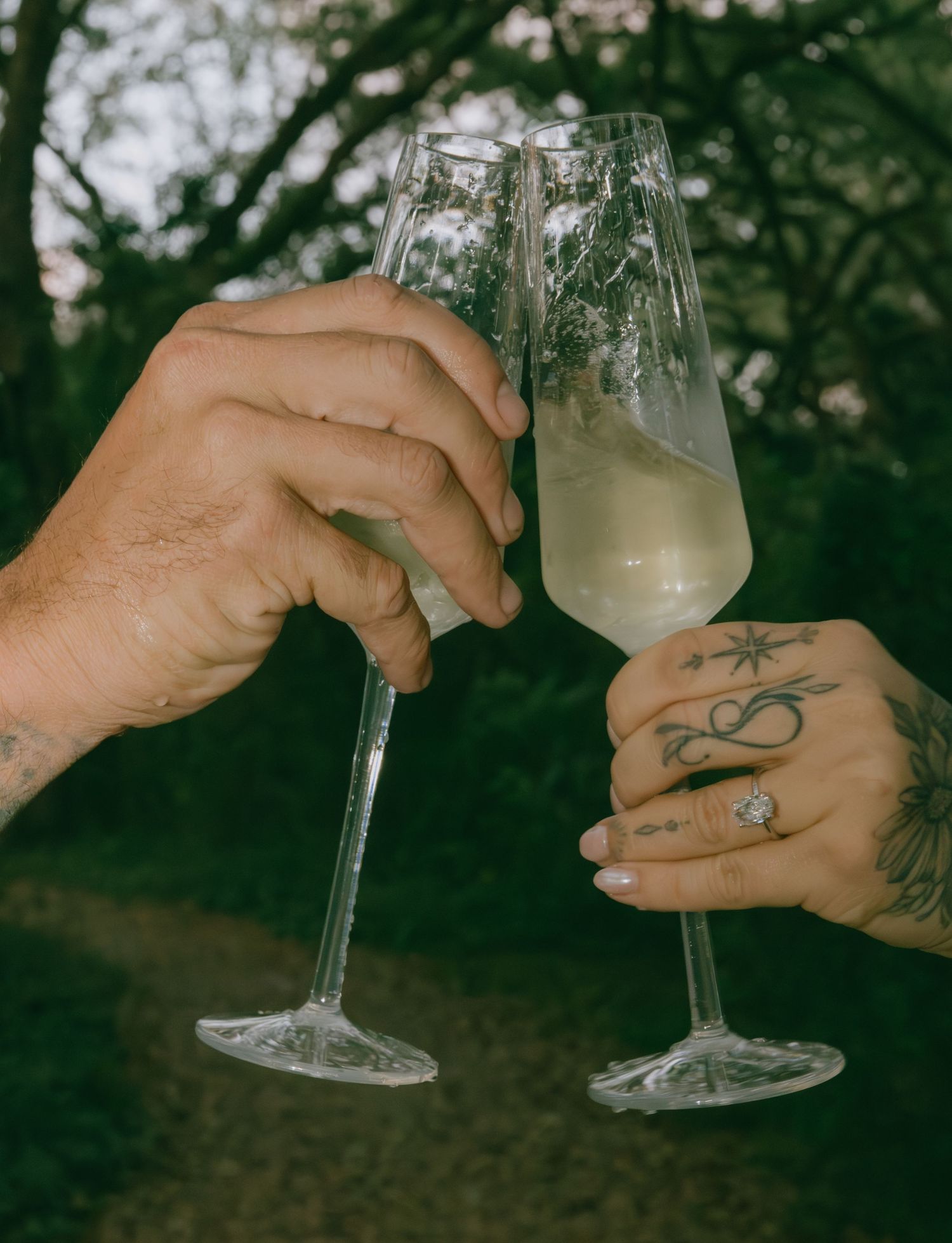 Two champagne glasses clinking together with tattooed hands.