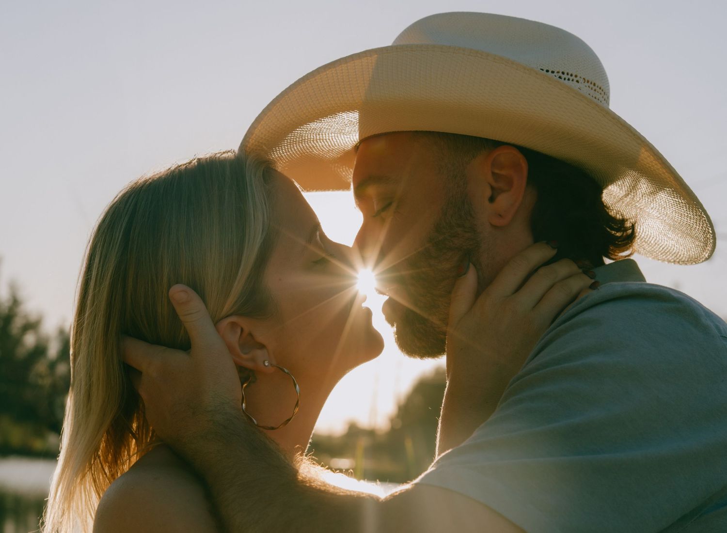 Three silhouetted figures wearing cowboy hats stand together at sunset with sunlight creating a warm backlit glow.