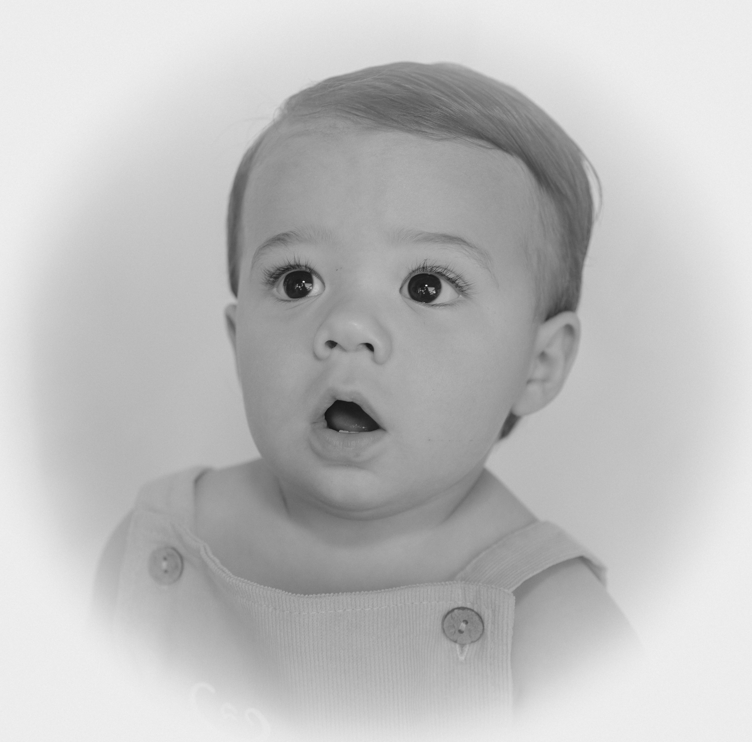 Black and white portrait of a baby with wide eyes and an open mouth wearing a button-up outfit.