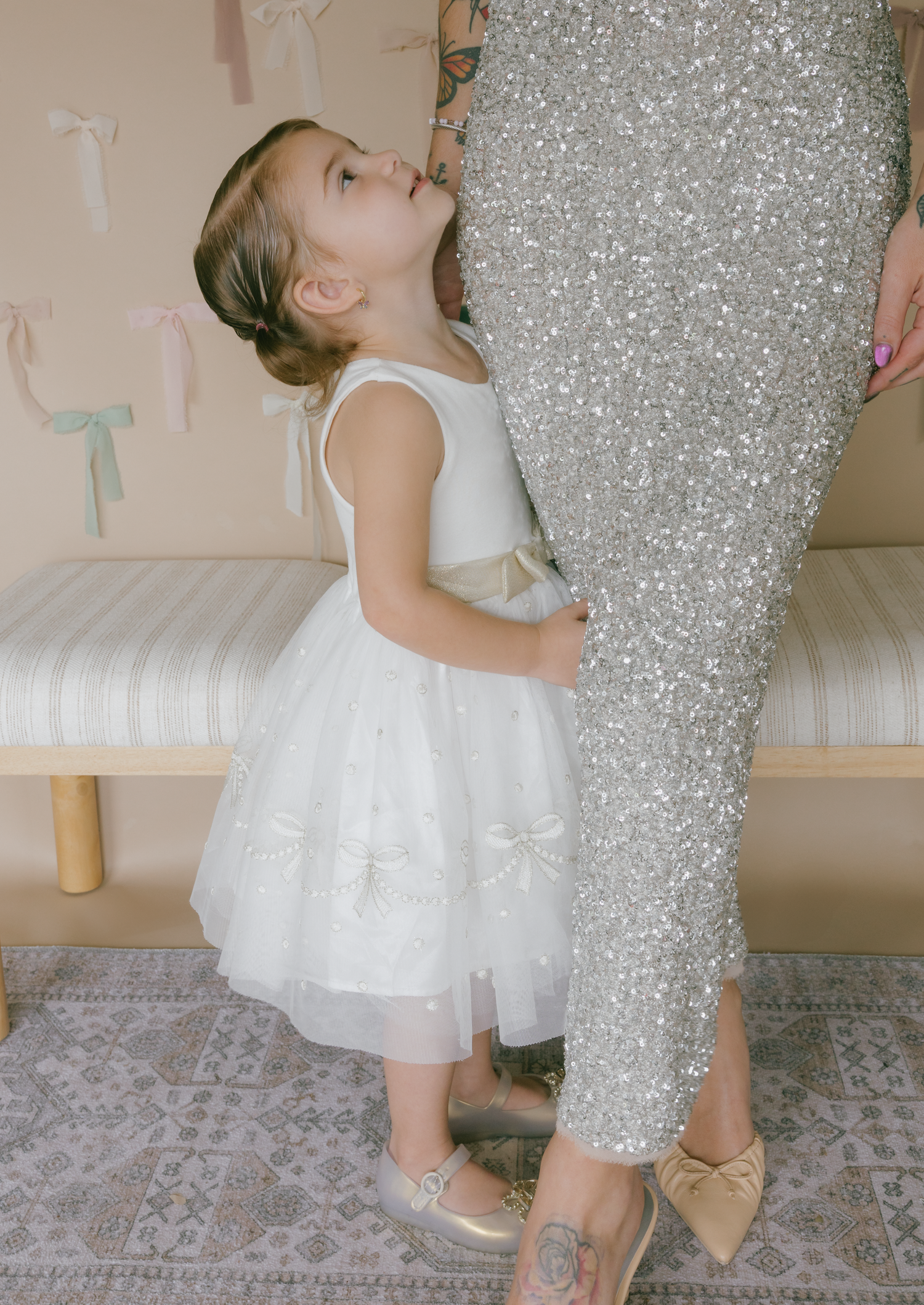 Small child in a white dress dances and twirls next to a sparkly silver Christmas tree.