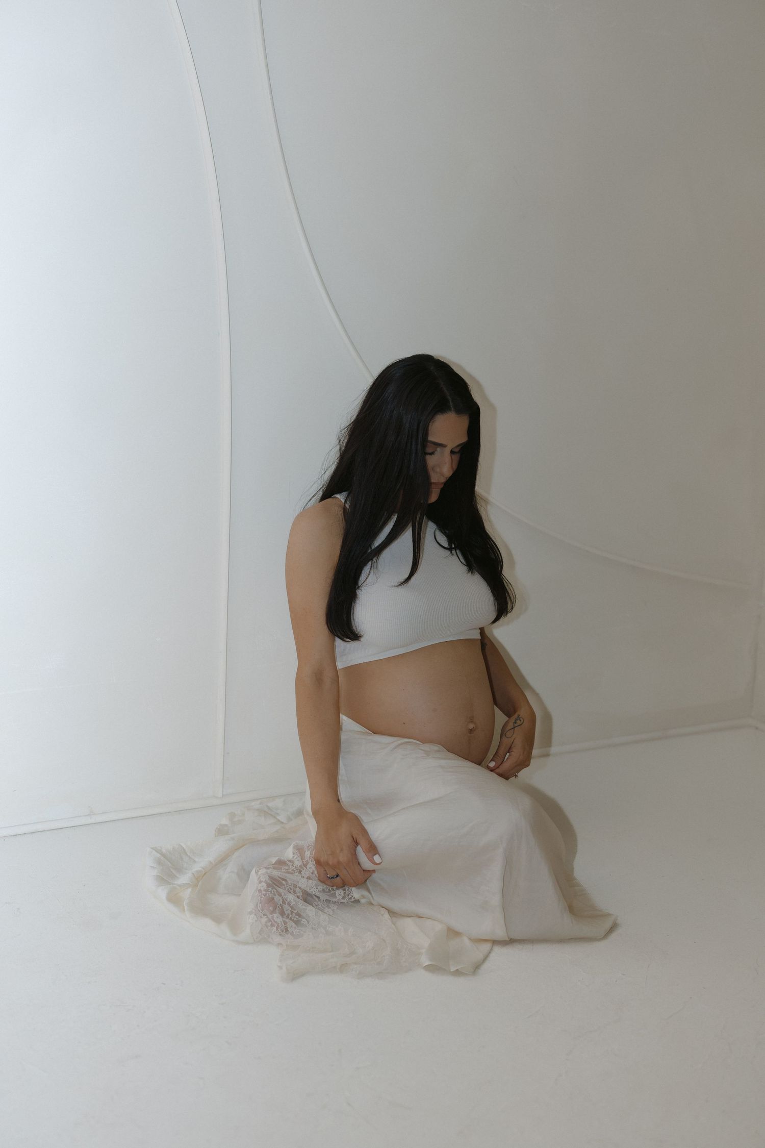 Artistic maternity photo series featuring a woman in white against a minimalist backdrop.