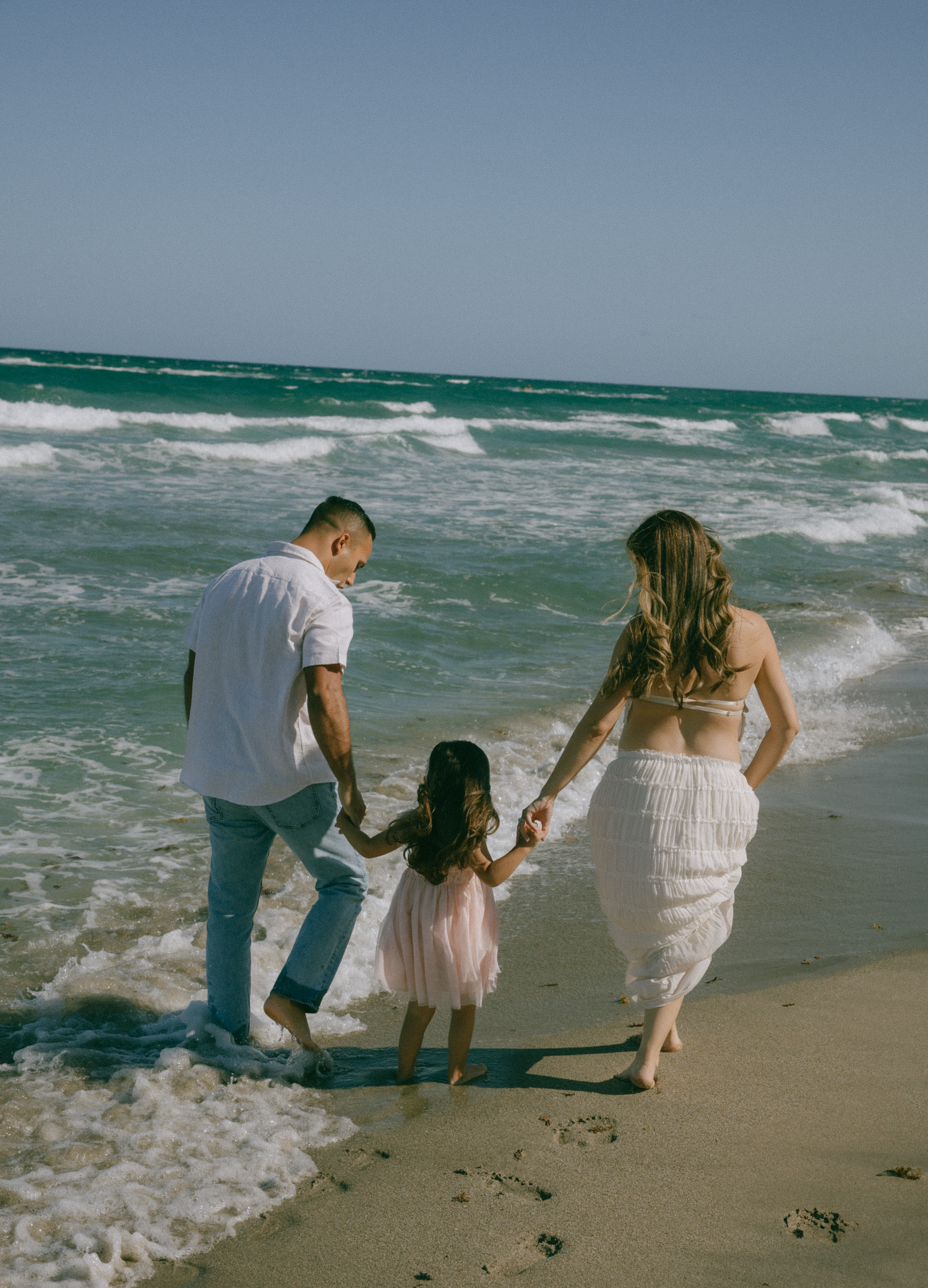 Family playing together on sandy beach with rolling waves.