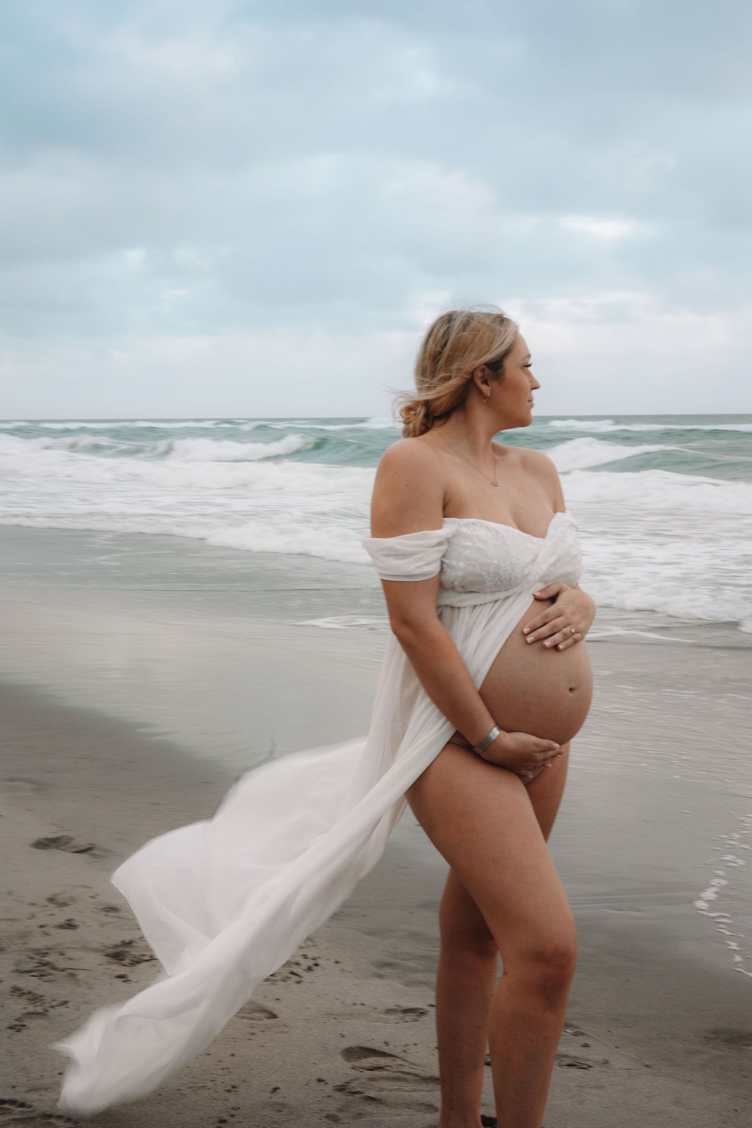 A flowing white dress billows in the ocean breeze on a cloudy beach.