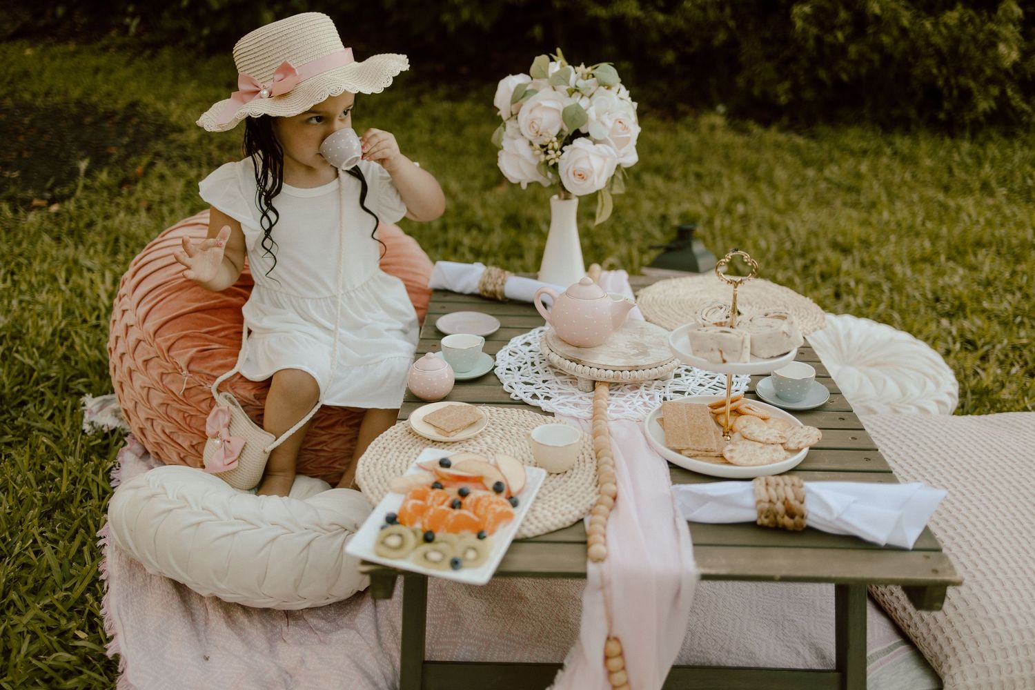 Elegant outdoor tea party setup with white florals and pink accents on rustic table.