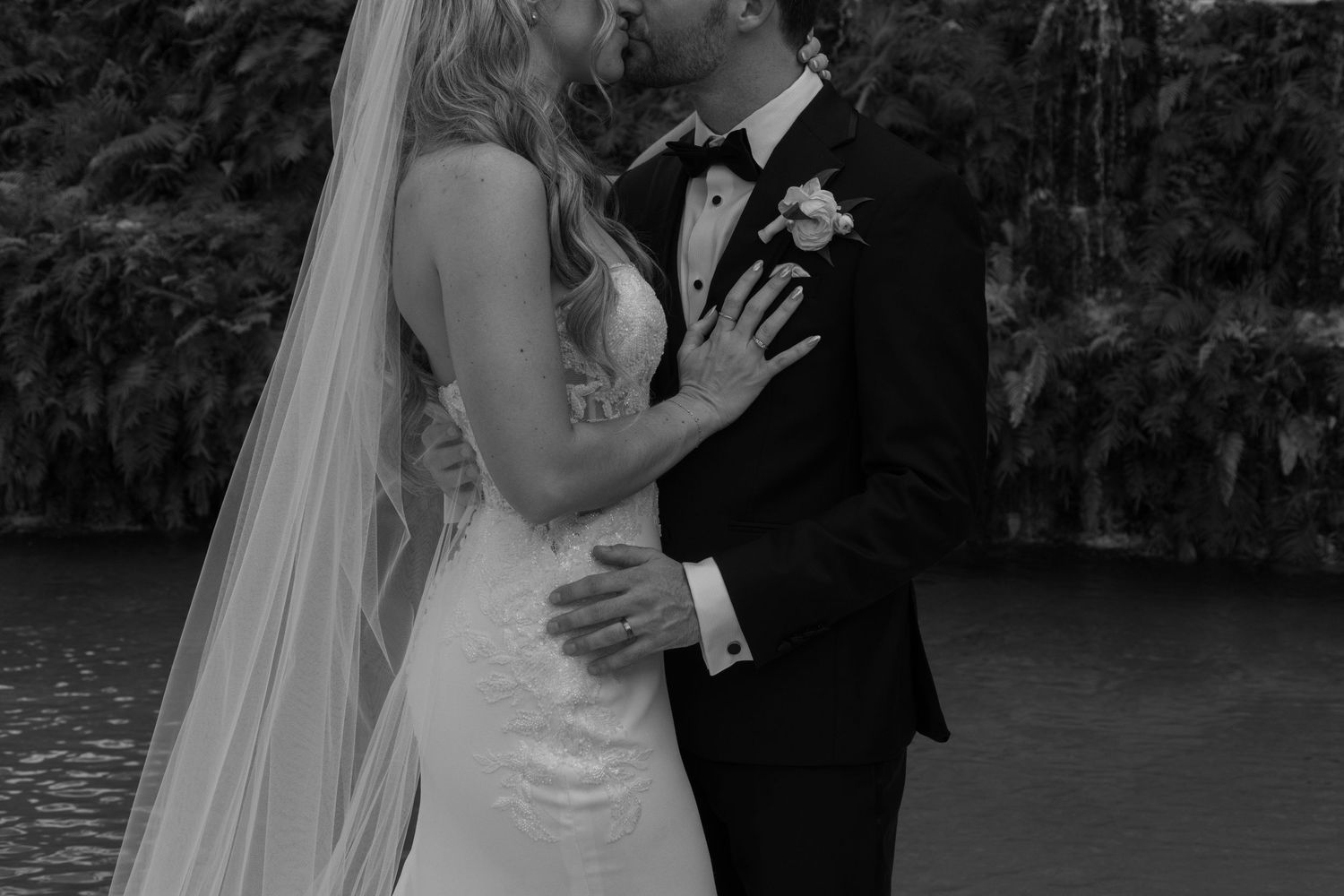 A romantic wedding couple embraces during their outdoor ceremony beside a lake at sunset.