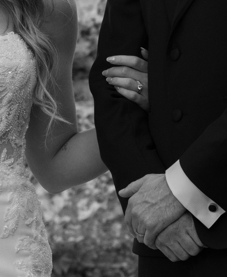Black and white wedding photo showing hands and arms of a bride in lace and groom in formal suit.