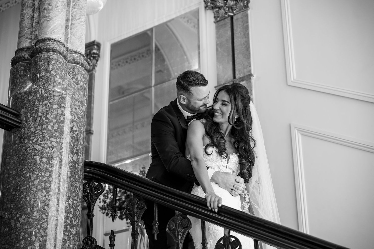 A romantic black and white wedding moment captured on an ornate staircase with marble columns in the background.