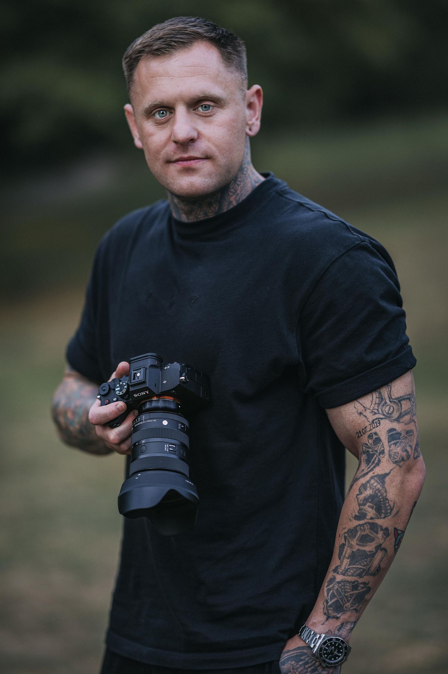 Photographer in black t-shirt with tattoos holding professional camera.