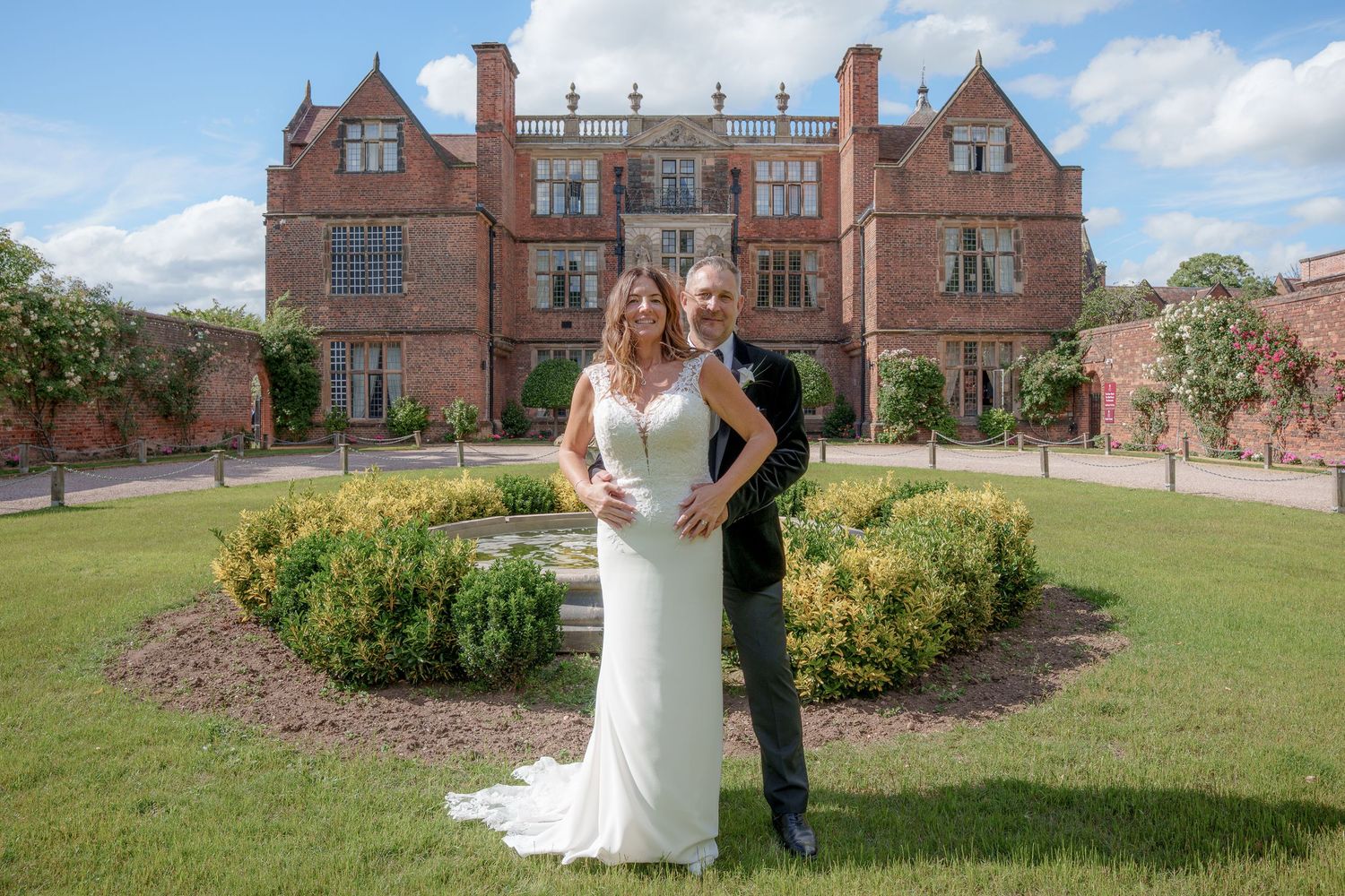 Bride and groom pose in front of a grand red brick manor house on their wedding day.
