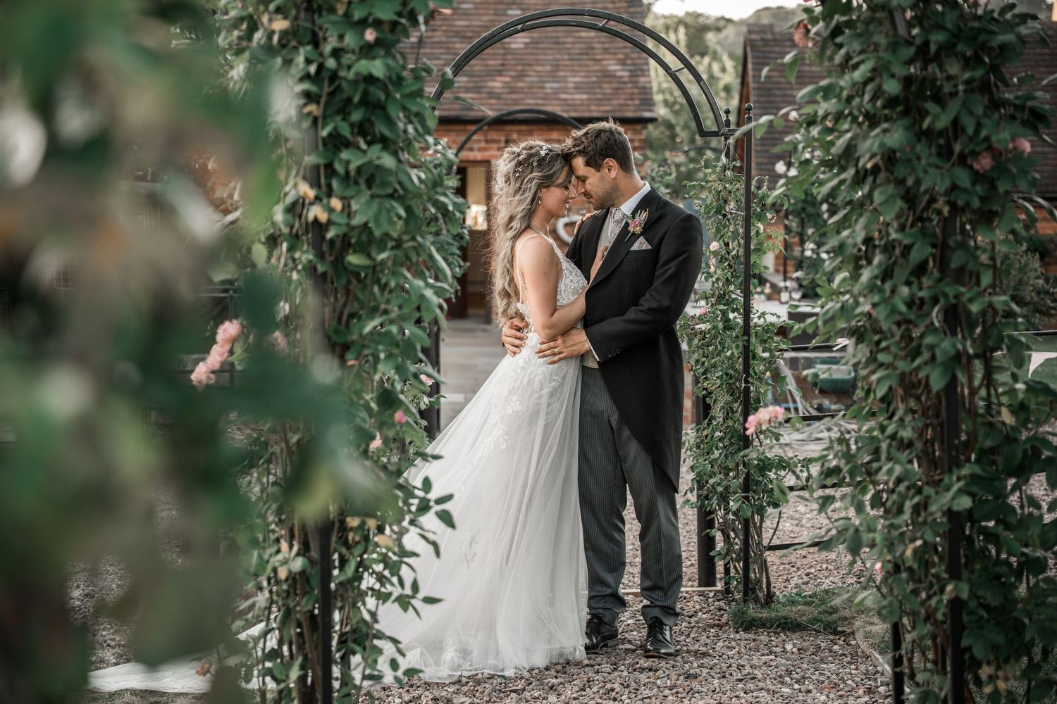 A romantic garden wedding moment under a vine-covered archway with lush greenery surrounds the couple.