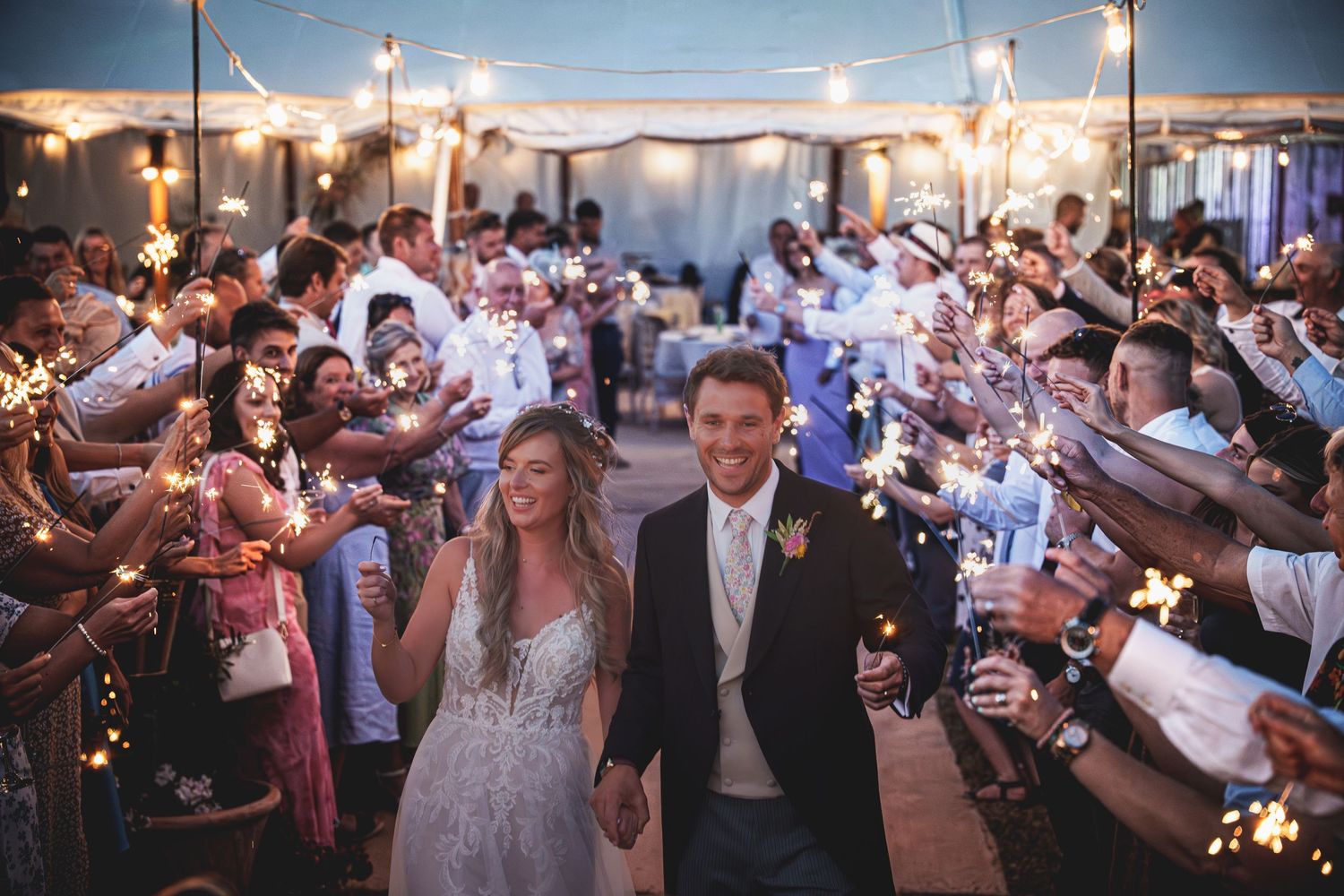 Sparklers illuminate a nighttime celebration as wedding guests line up to send off the newlyweds in a magical display.