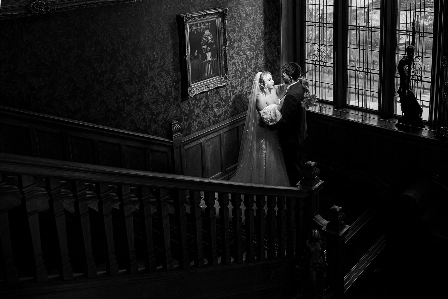 Bride and groom share a romantic moment on a grand staircase in a stunning black and white wedding photo.
