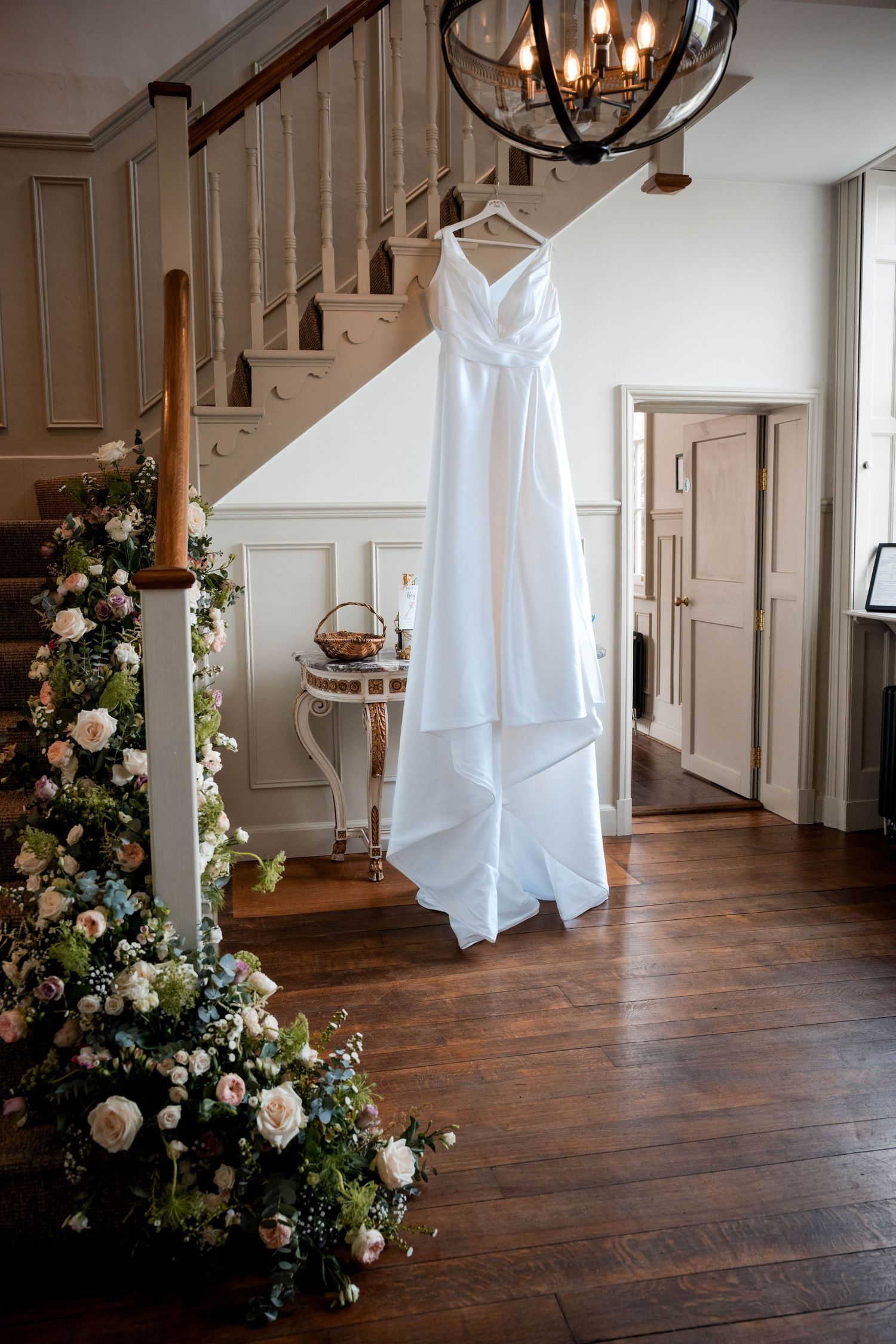 White wedding dress hanging in an elegant indoor space with hardwood floors and floral arrangements.
Stockton house wedding venue