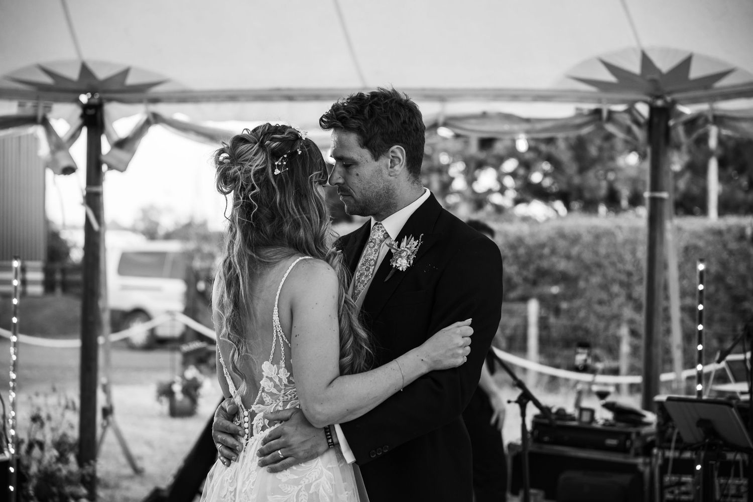 A couple embraces while dancing together at an outdoor wedding reception with scenic views of trees and water.