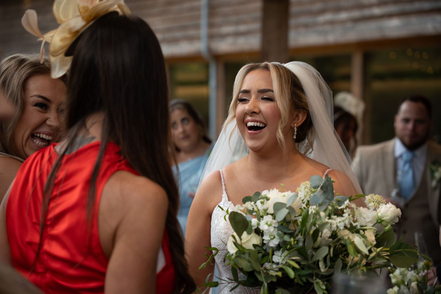 A bride wearing white holds a bouquet while sharing a laugh with wedding guests outdoors.
The Mill Barns wedding venue
