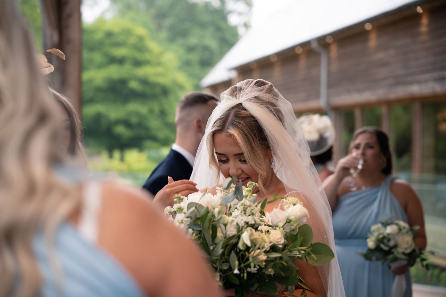 A bride holding a white and green bouquet shares a joyful moment with wedding guests.
The Mill Barns wedding venue