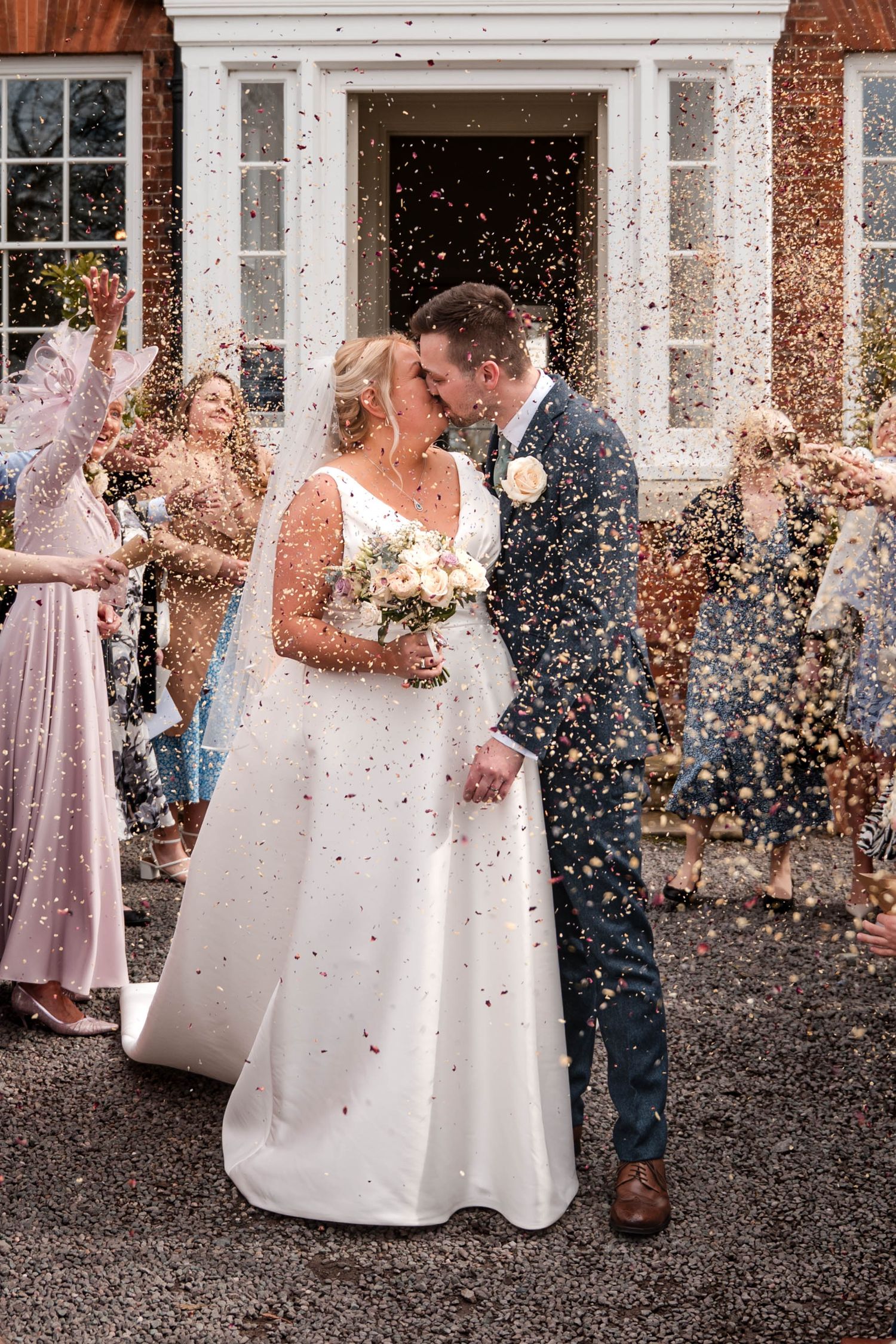 Wedding celebration scene with confetti being thrown outside brick building entrance.
