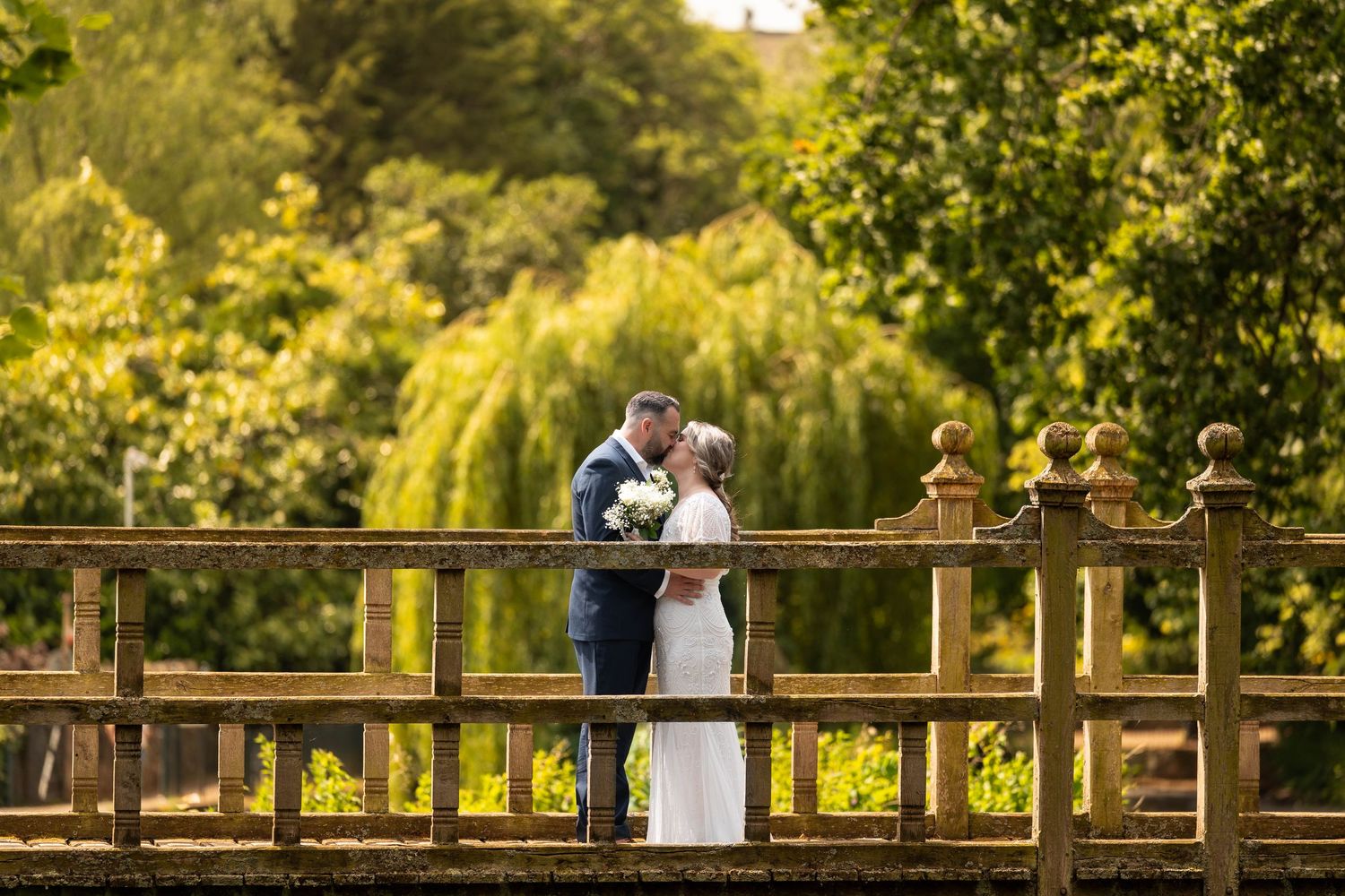 Wedding couple strolls along wooden bridge surrounded by lush green foliage.
Malvern hills council house wedding venue