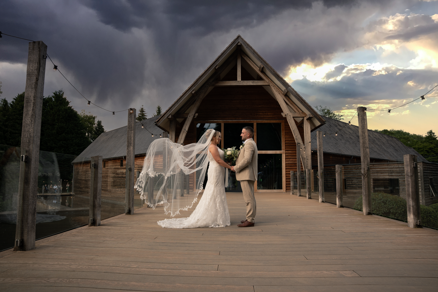Wedding couple silhouetted against dramatic stormy sky at sunset on rustic wooden deck.