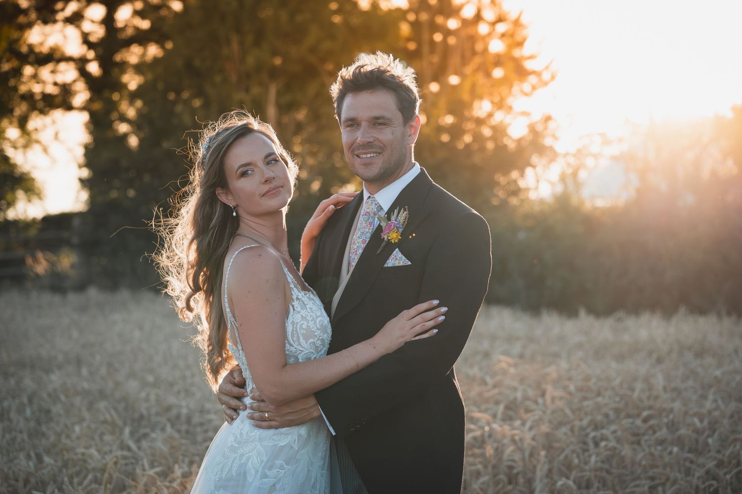 A romantic wedding couple embraces in a sun-drenched field at golden hour with soft lighting and natural scenery.