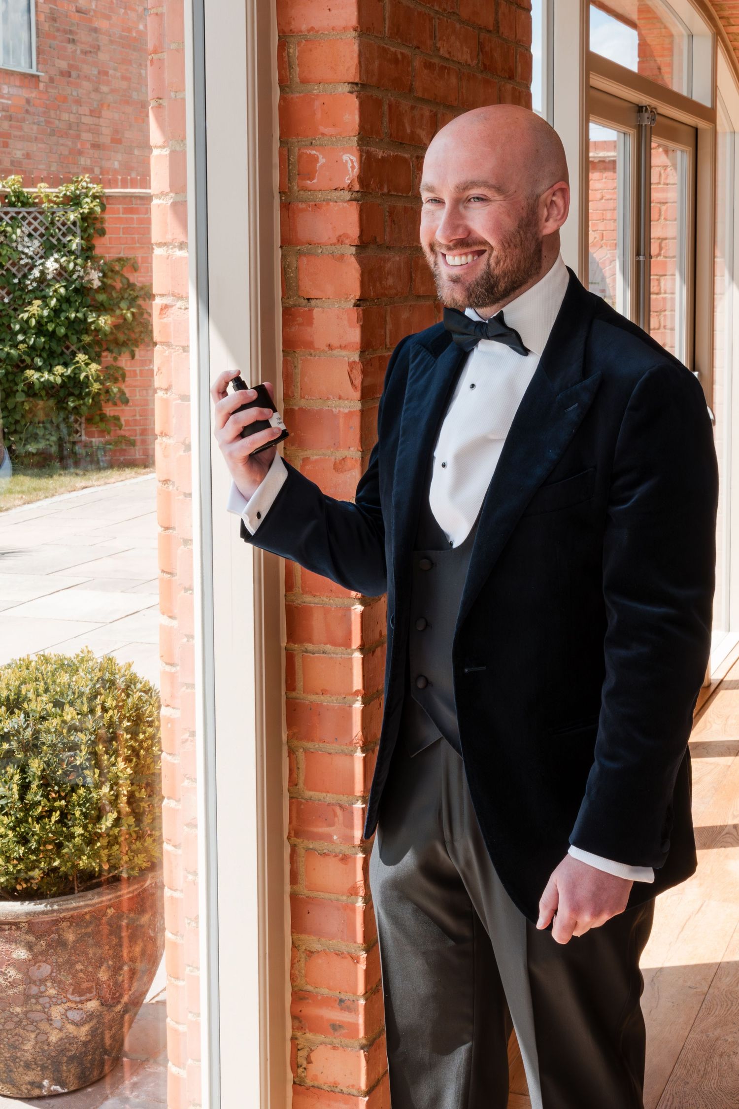 Groom in classic tuxedo smiling by brick wall with natural window light.
Cider mill barns wedding venue