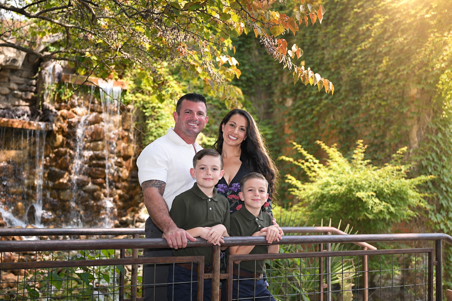 Family of four smiling on a bridge with a waterfall and lush greenery in the background.