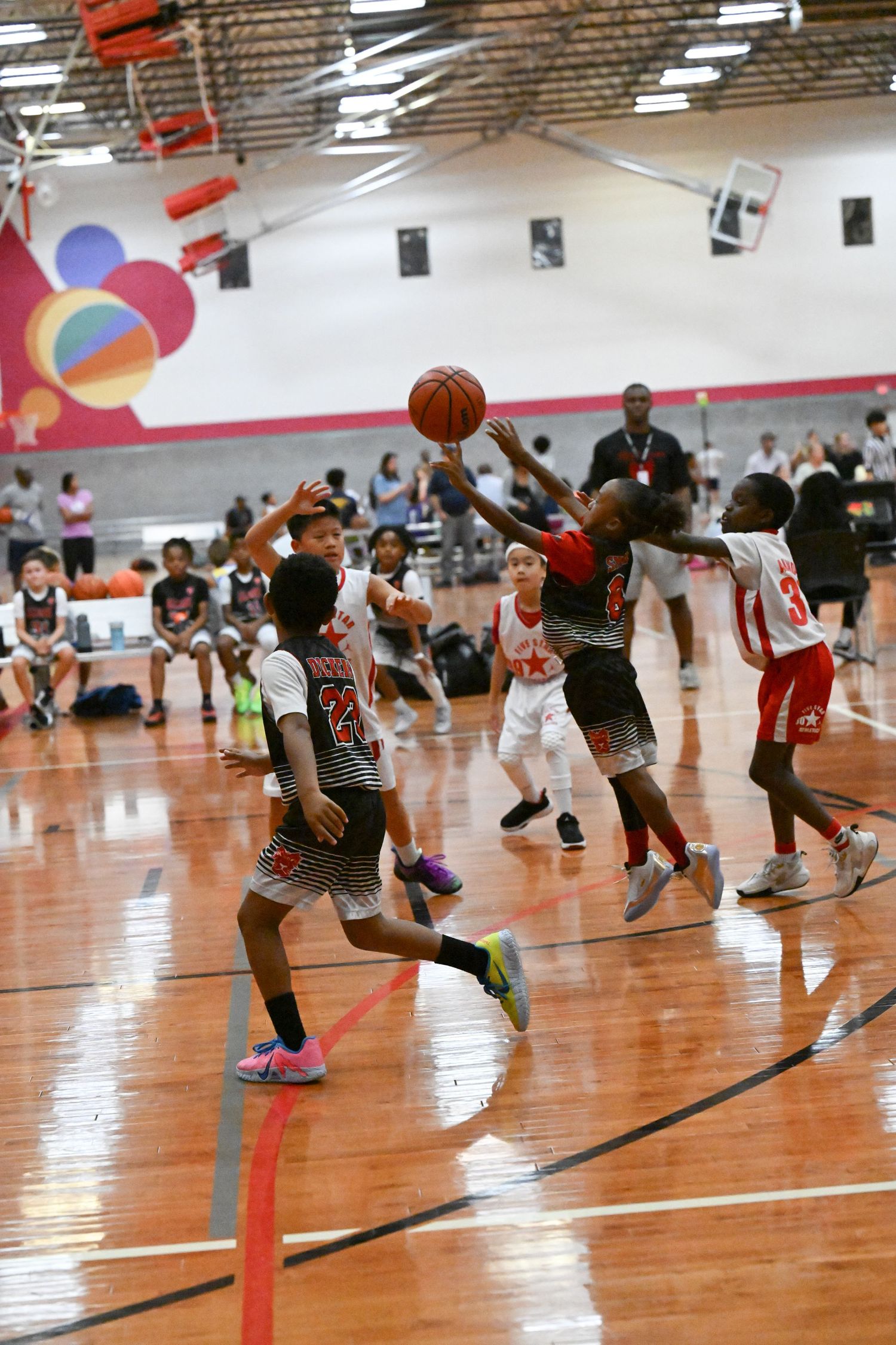 Young basketball players compete in an indoor youth basketball game on a shiny hardwood court.