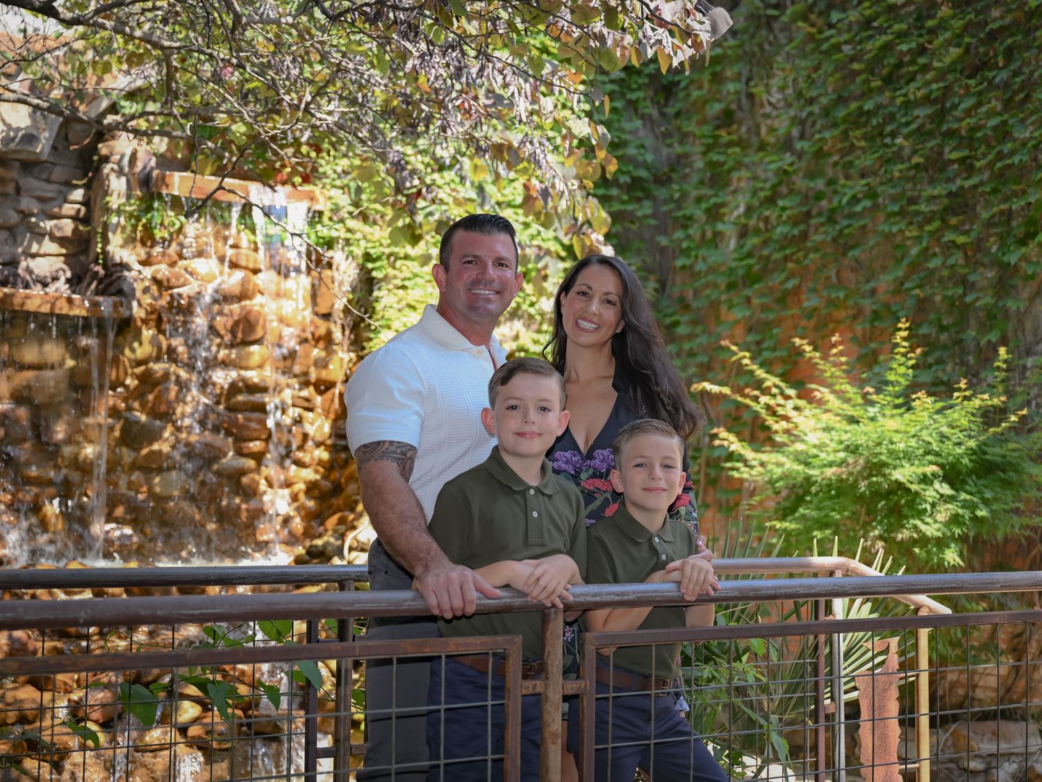 Family of four posing on a bridge near a beautiful stone waterfall outdoors.