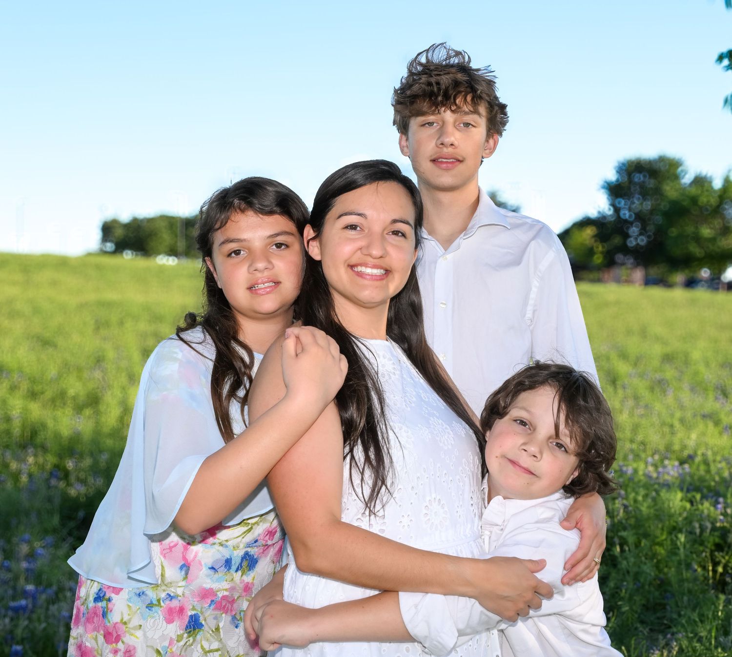 Four children pose together smiling in a green field on a sunny day.