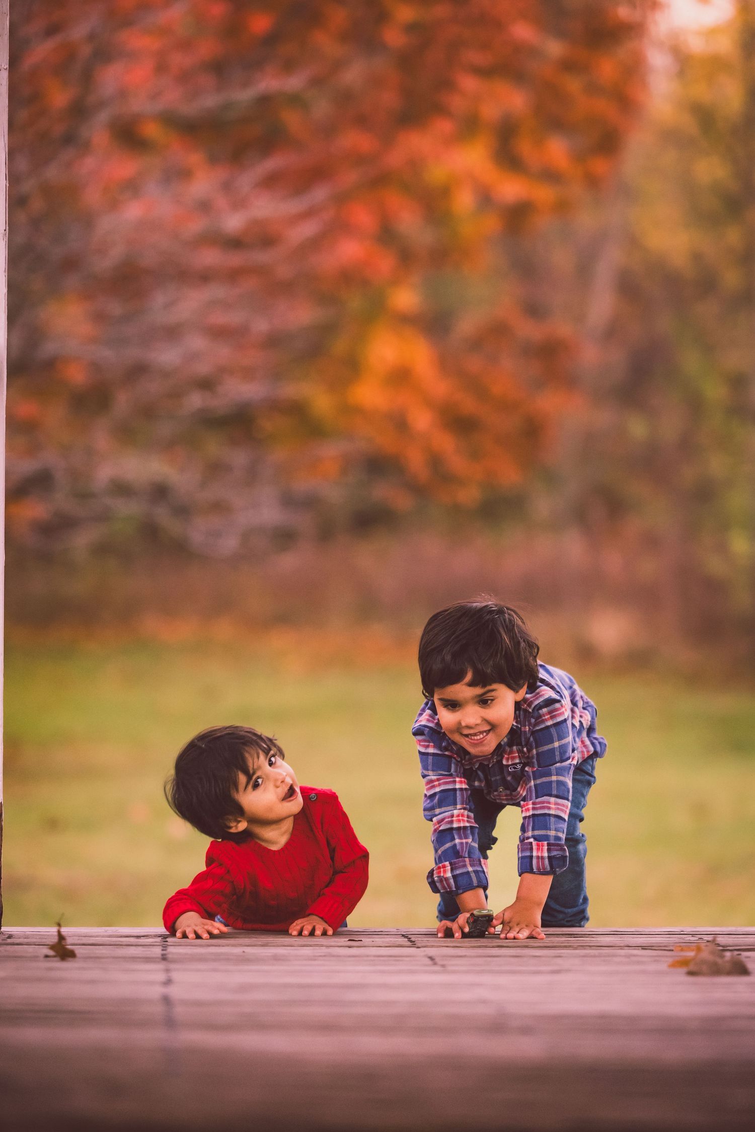 Two children peek over a wooden surface with playful expressions against a warm autumn background.