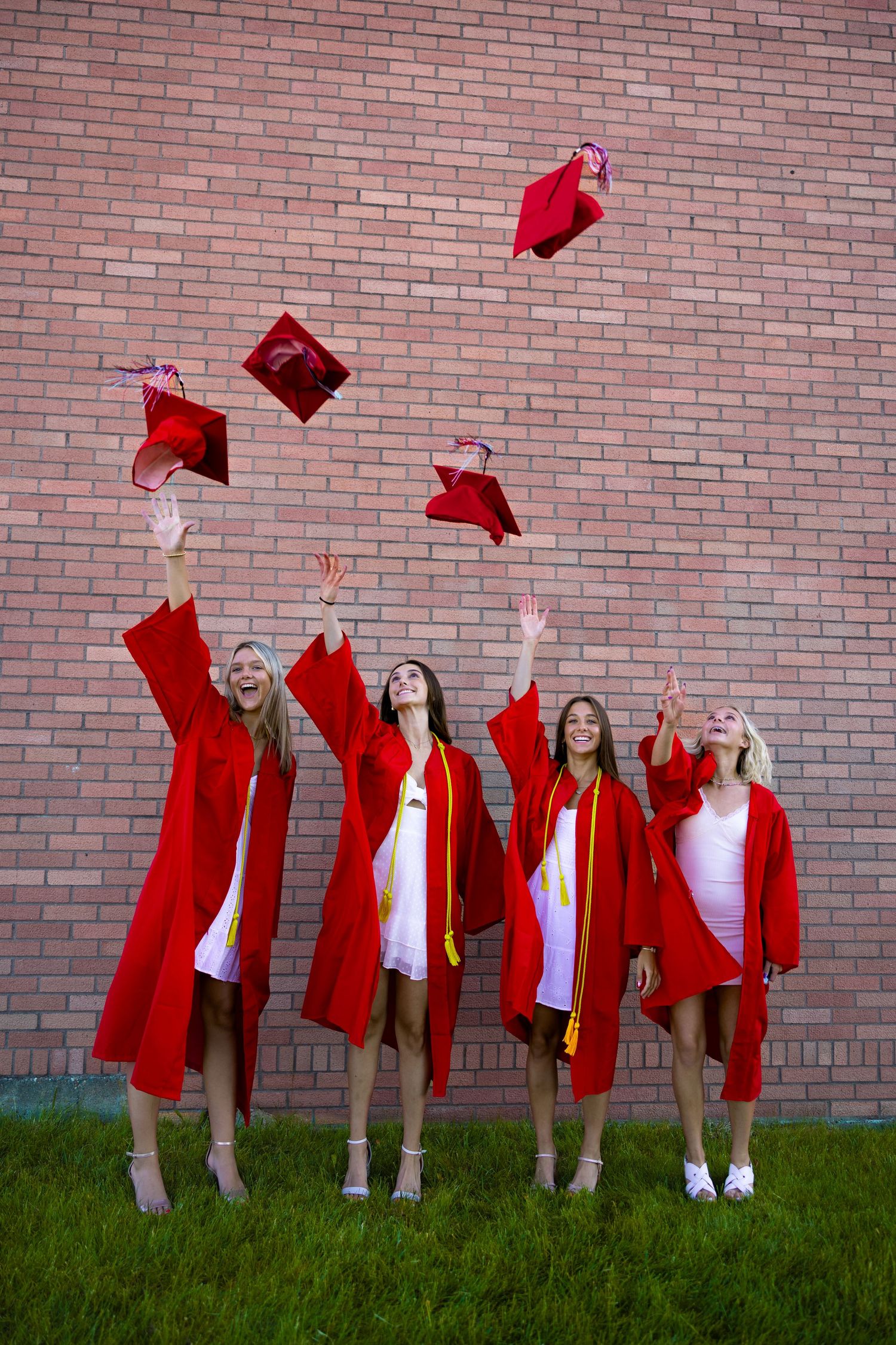 Group of graduates throwing red caps in celebration against brick wall.