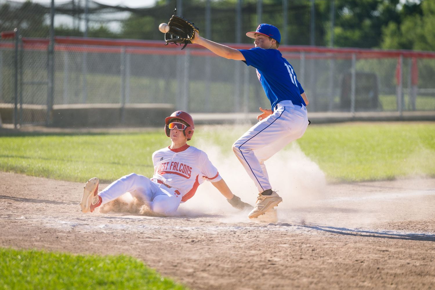 Baseball player sliding into home plate creating dust cloud during game.