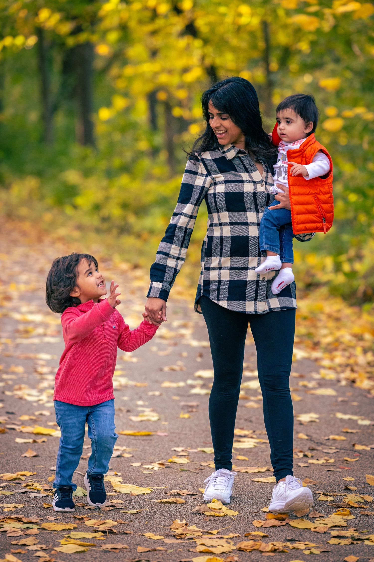 Parent and child interact playfully among fallen autumn leaves on a forest path.