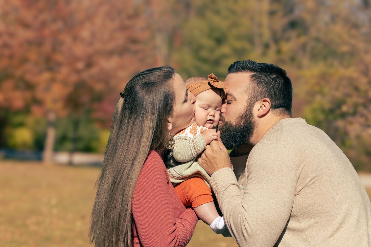 A tender family moment captured outdoors during autumn with warm lighting and fall colors.