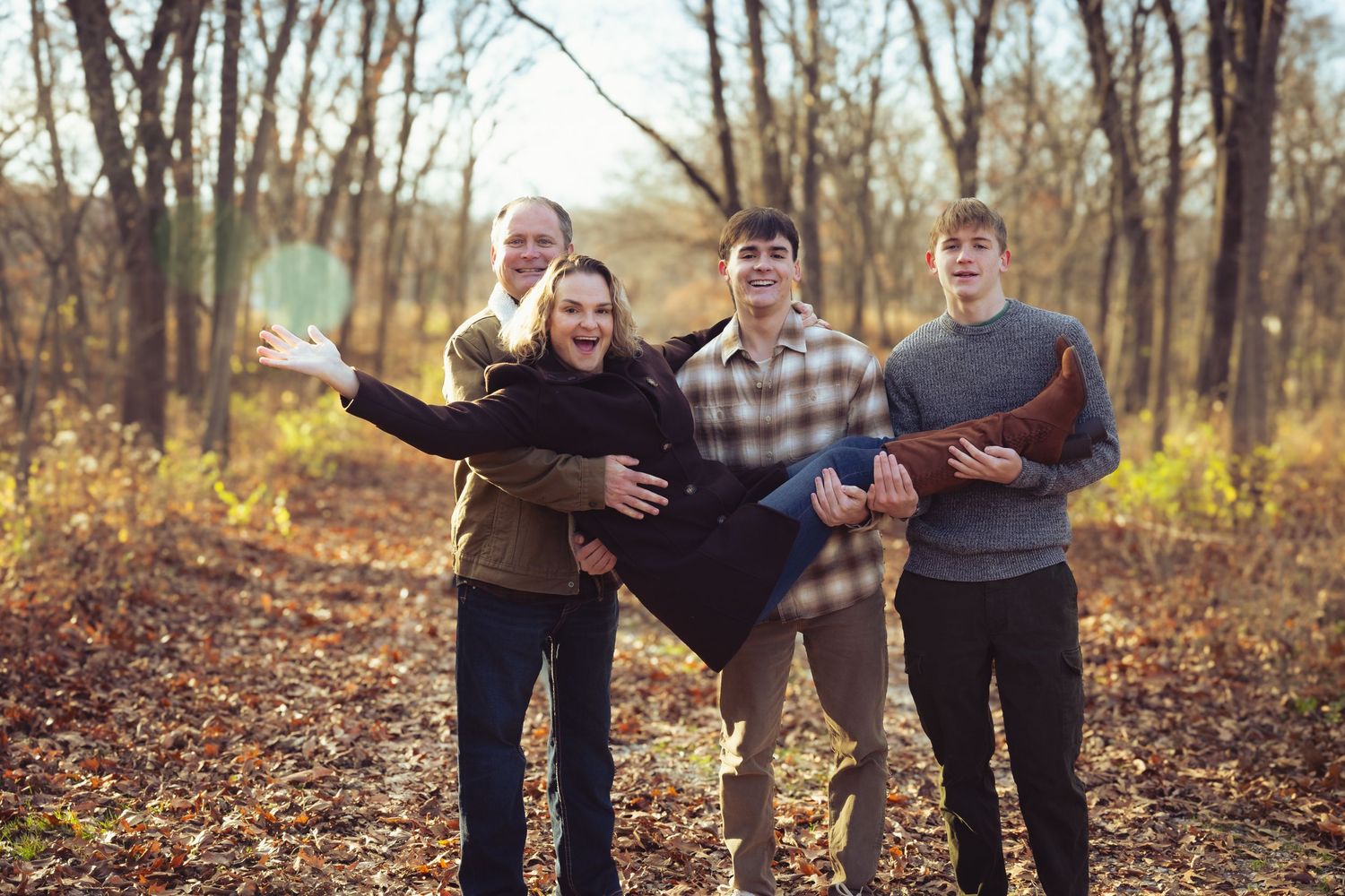 Three people pose playfully together on fallen autumn leaves in a wooded area.