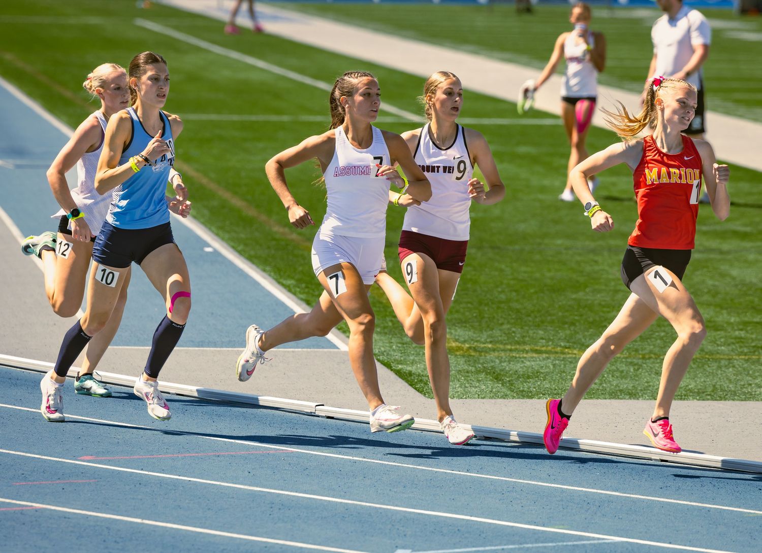 Athletes running on a blue track during a competitive race.
