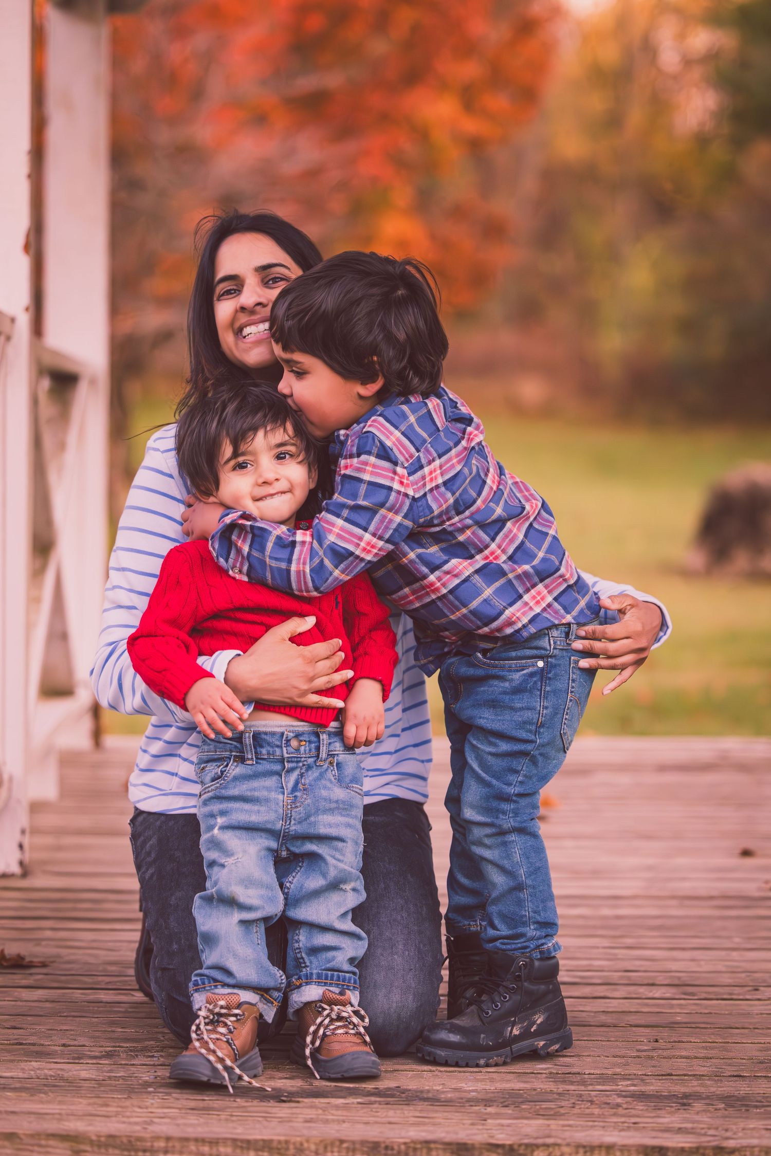 A family shares a warm embrace on a wooden deck during a beautiful autumn day with colorful fall foliage in the background.