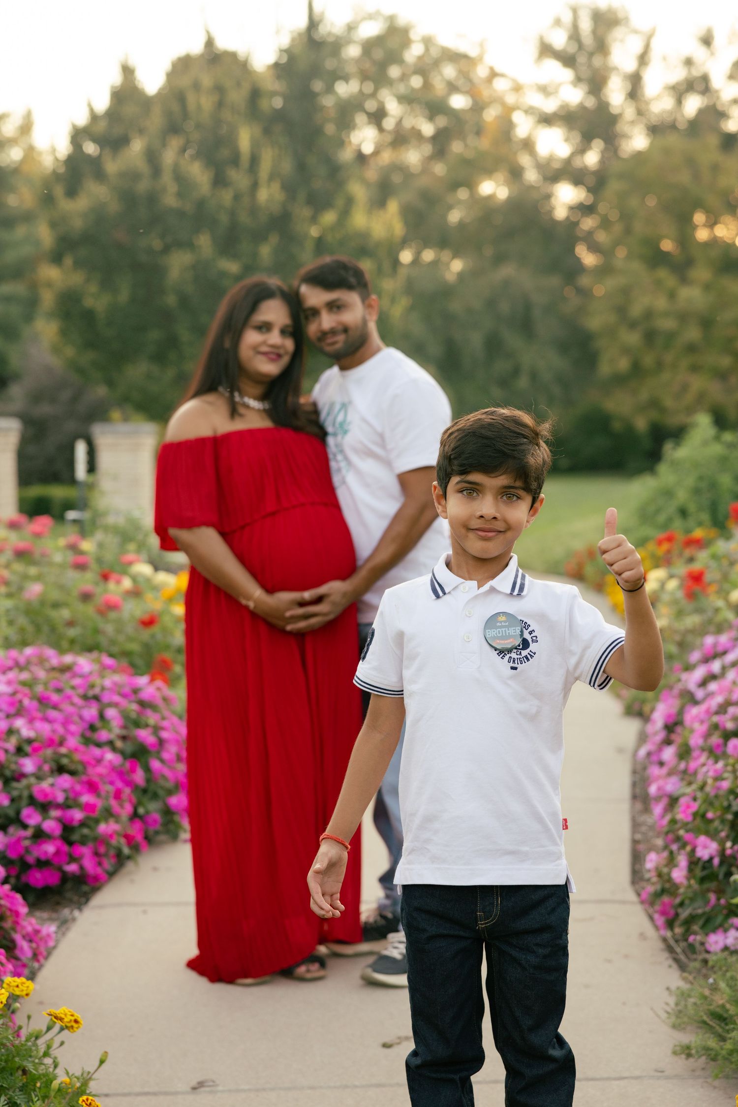 A family poses in a garden path surrounded by colorful pink and red flowers in bloom.