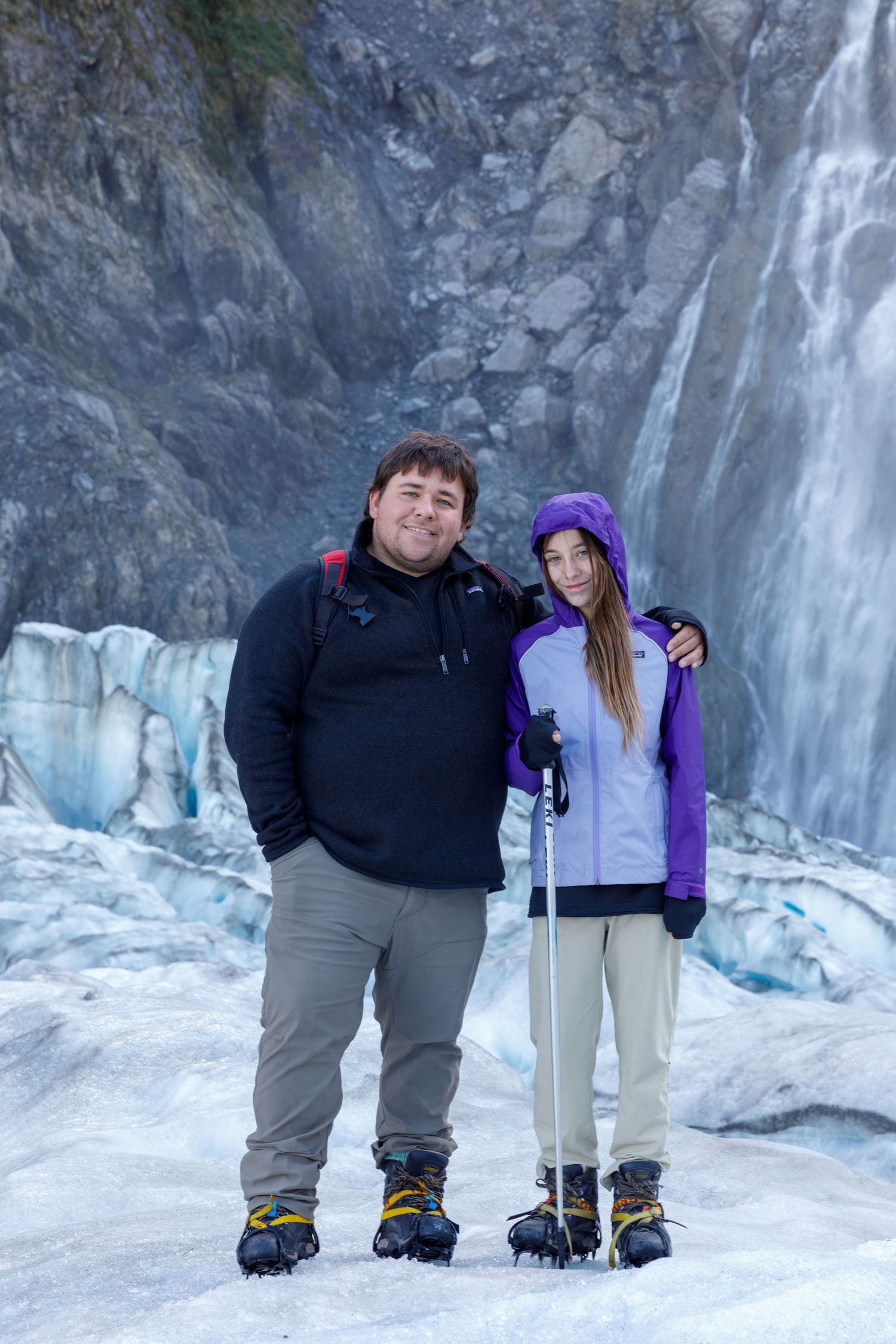 Group of hikers pose in front of a frozen waterfall and icy cliffs in winter.